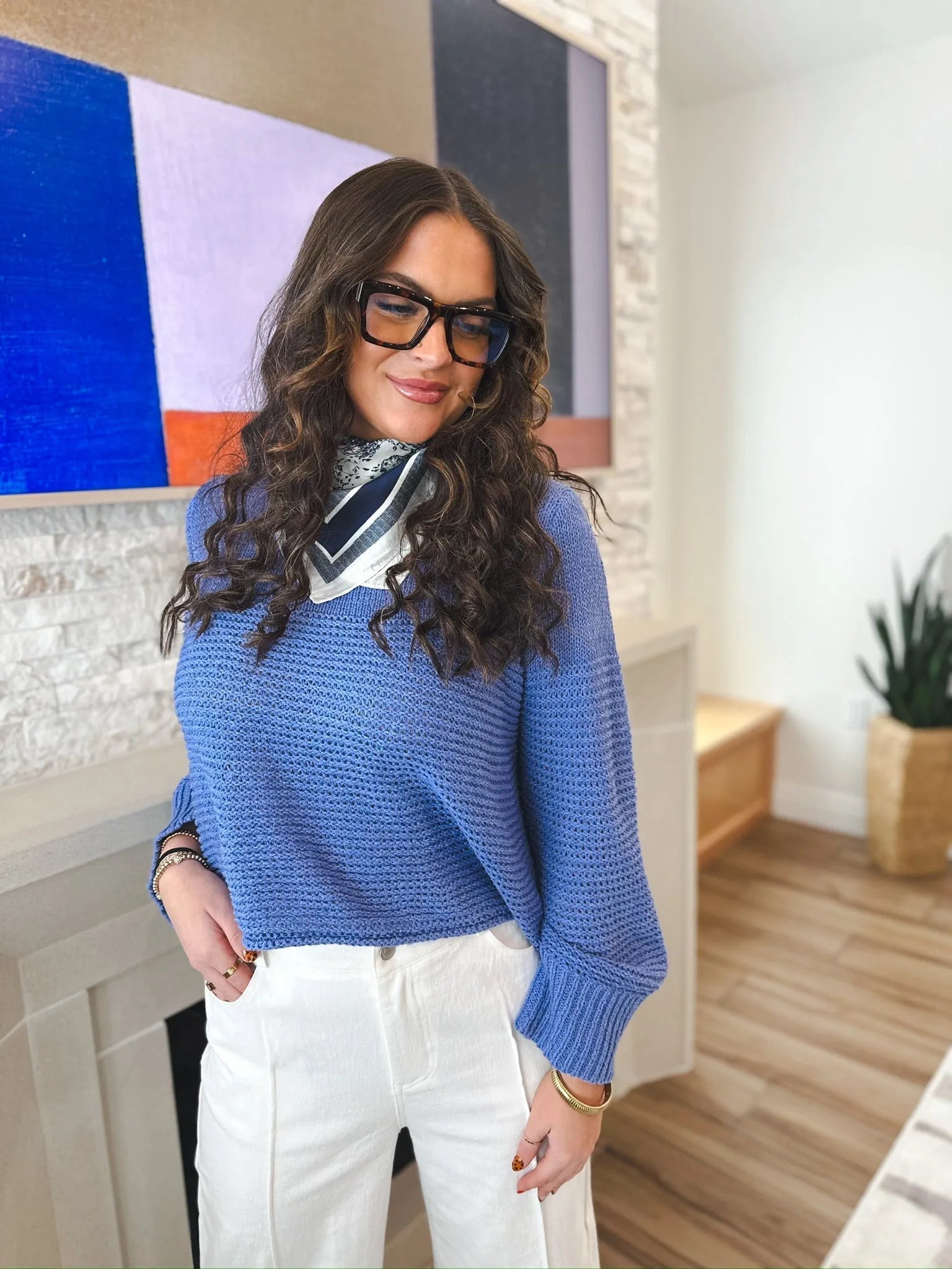 Entro periwinkle blue knit sweater with crew neck and long sleeves, worn with white pants and a printed scarf.