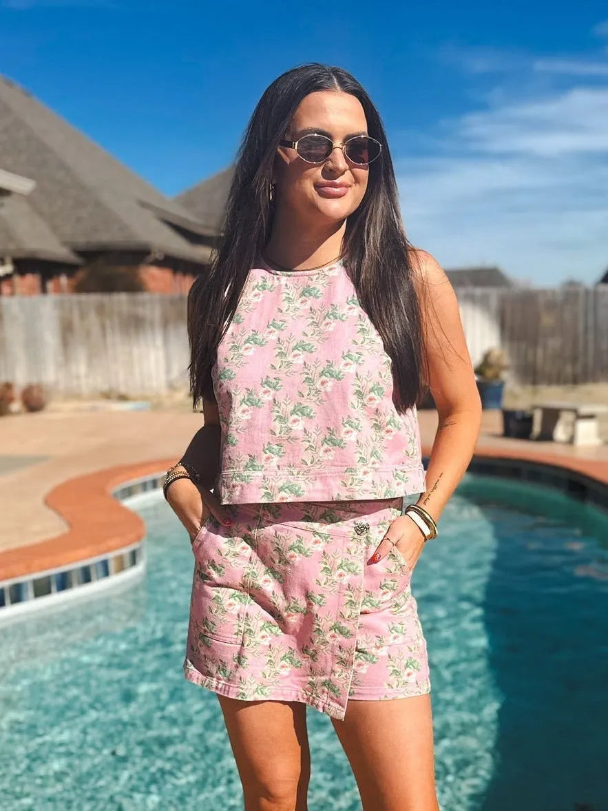 Woman wearing a pink floral denim skort and matching halter tank top outdoors by a pool.