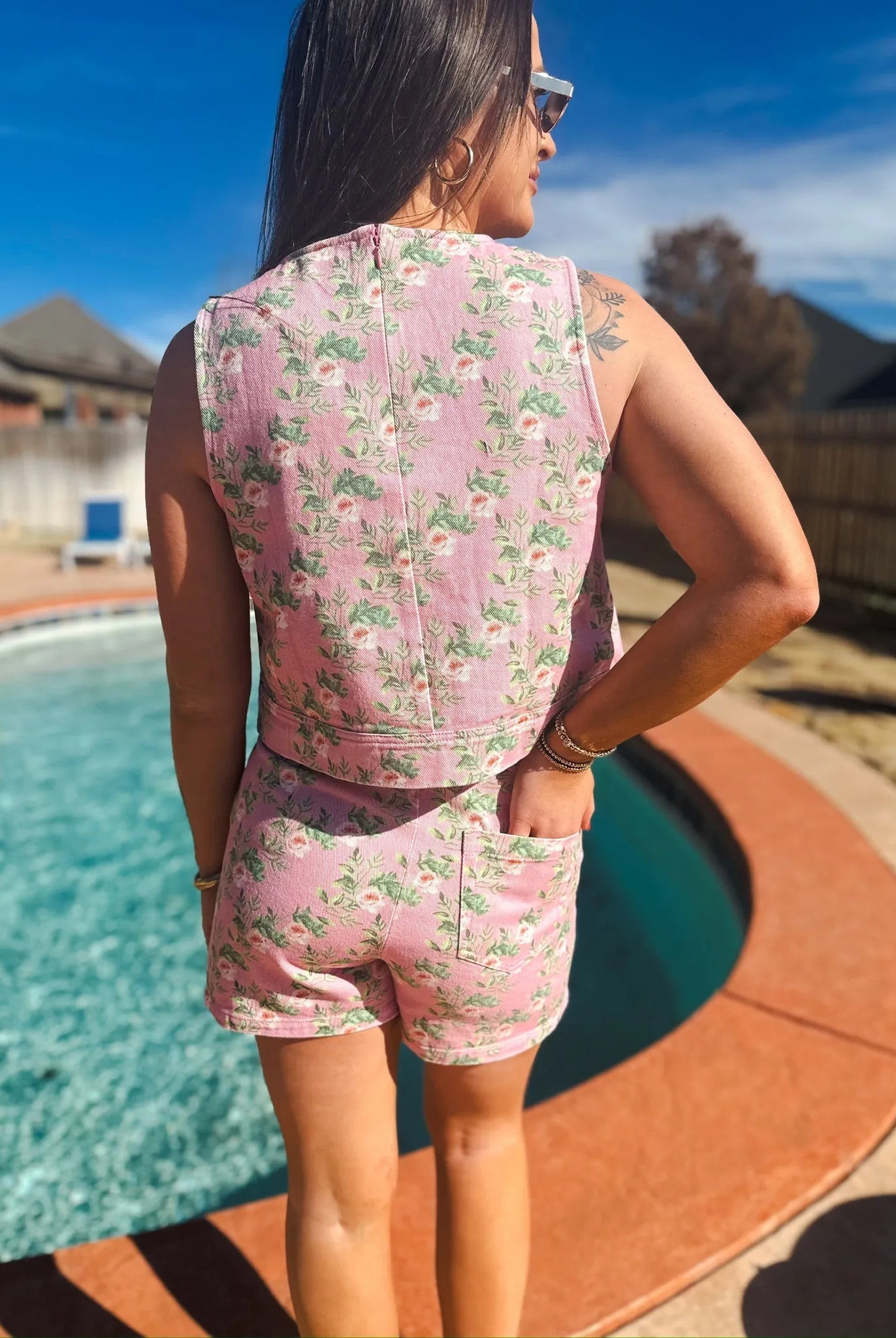 Woman wearing a pink floral denim skort and sleeveless tank top set, standing by a pool.