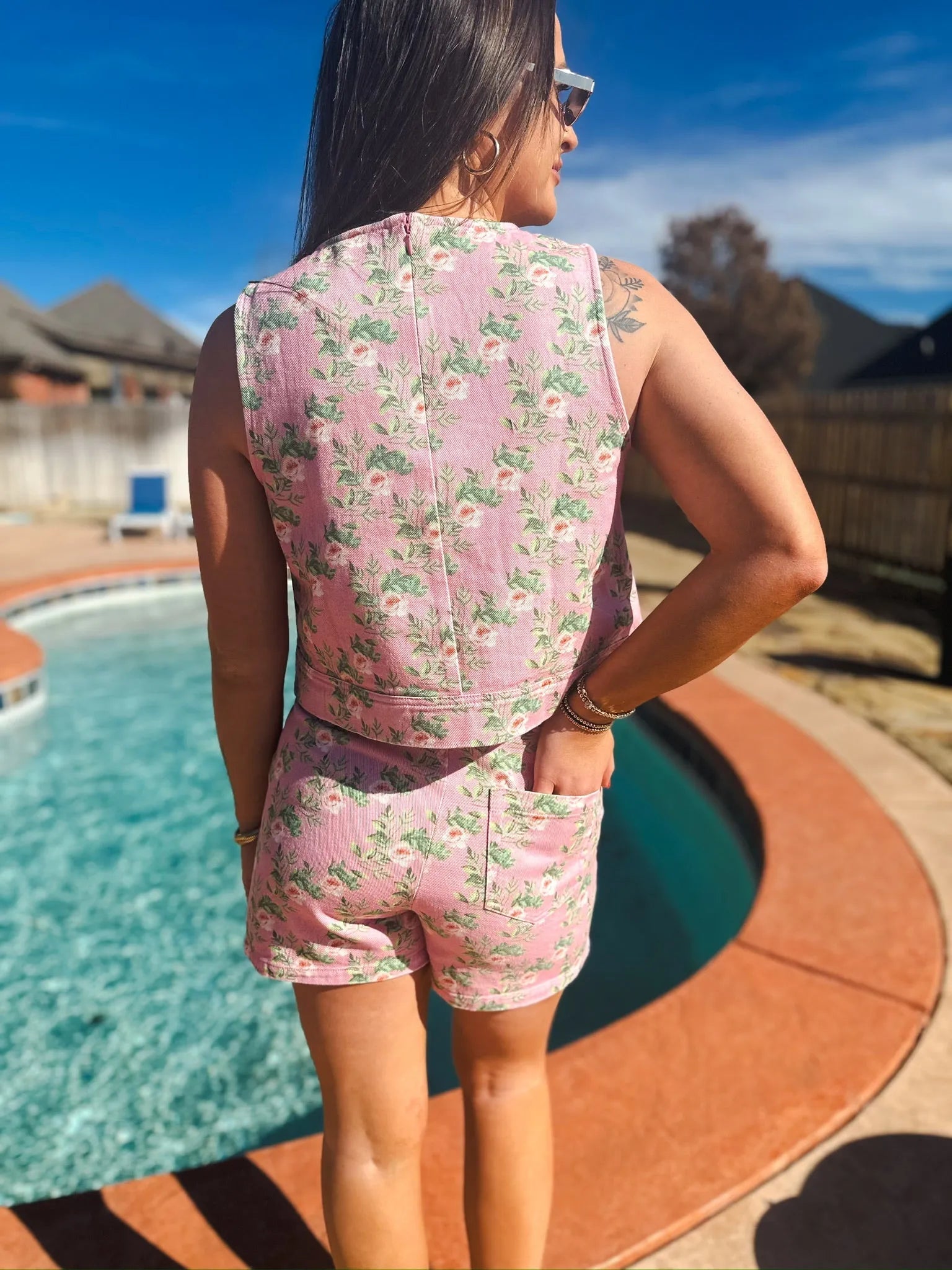 Woman wearing a pink floral denim skort and sleeveless tank top set, standing by a pool.