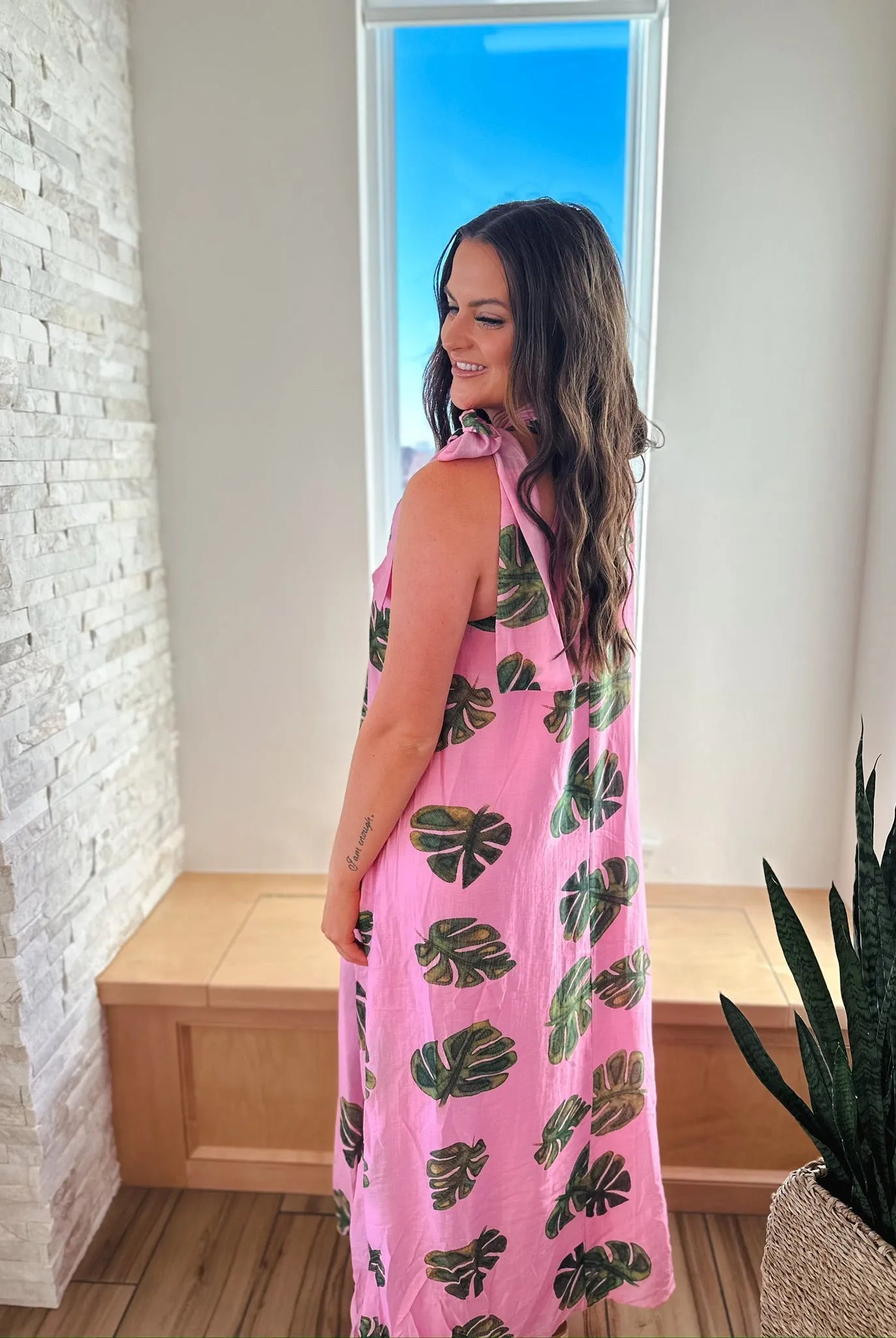 Entro pink maxi dress with green palm leaf print and tie neck. Woman wearing the dress from the back.