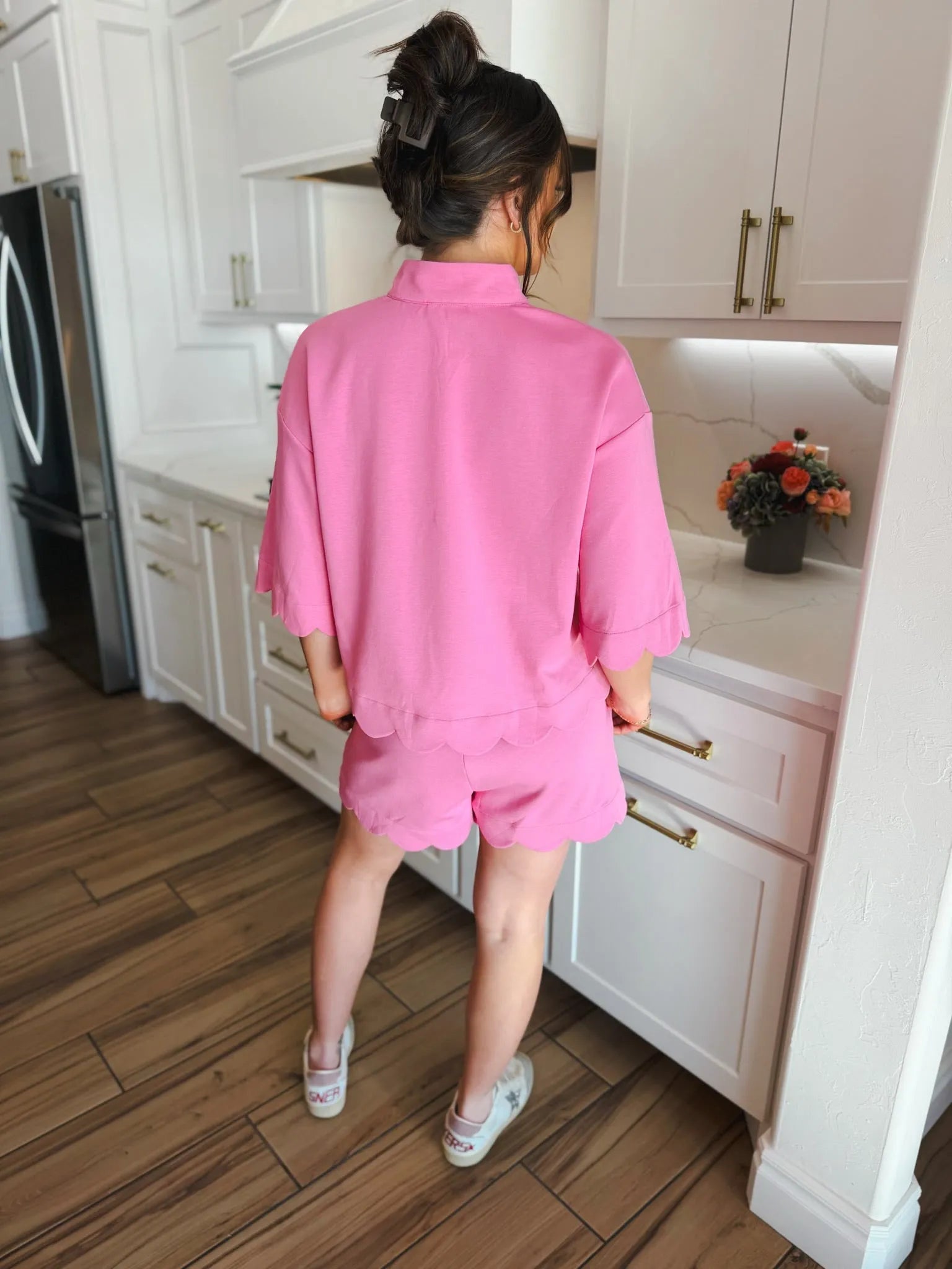 Woman wearing a pink scalloped short and top set, featuring a relaxed fit and decorative hemline. Standing in a modern