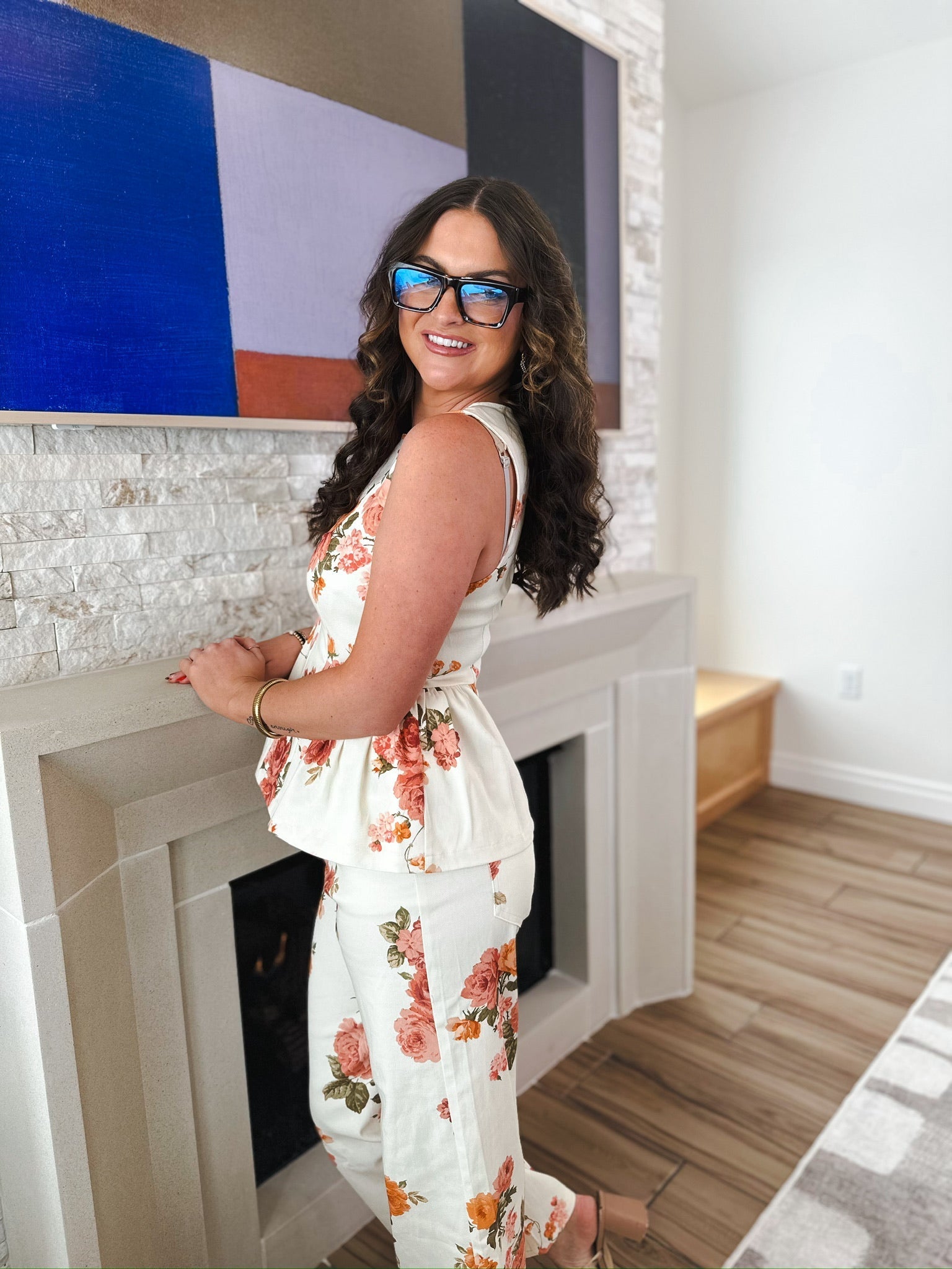 Woman wearing a white floral print peplum top and matching pants. The outfit has a peplum waist and a zip back closure.
