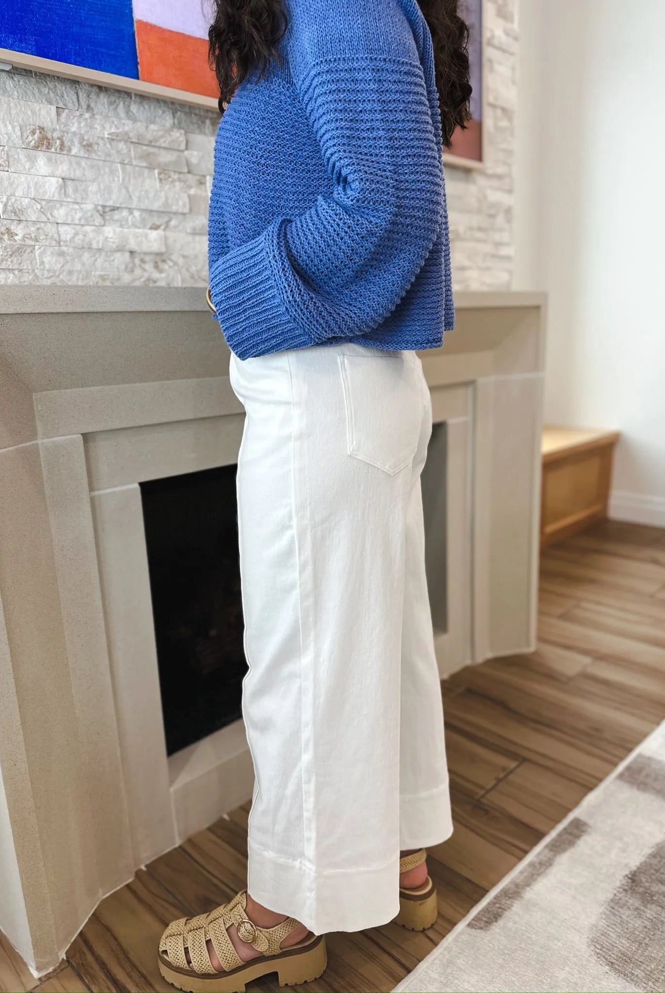 Entro white denim wide leg jeans with pleats, featuring a relaxed fit and a back pocket. Woman wearing blue sweater and tan