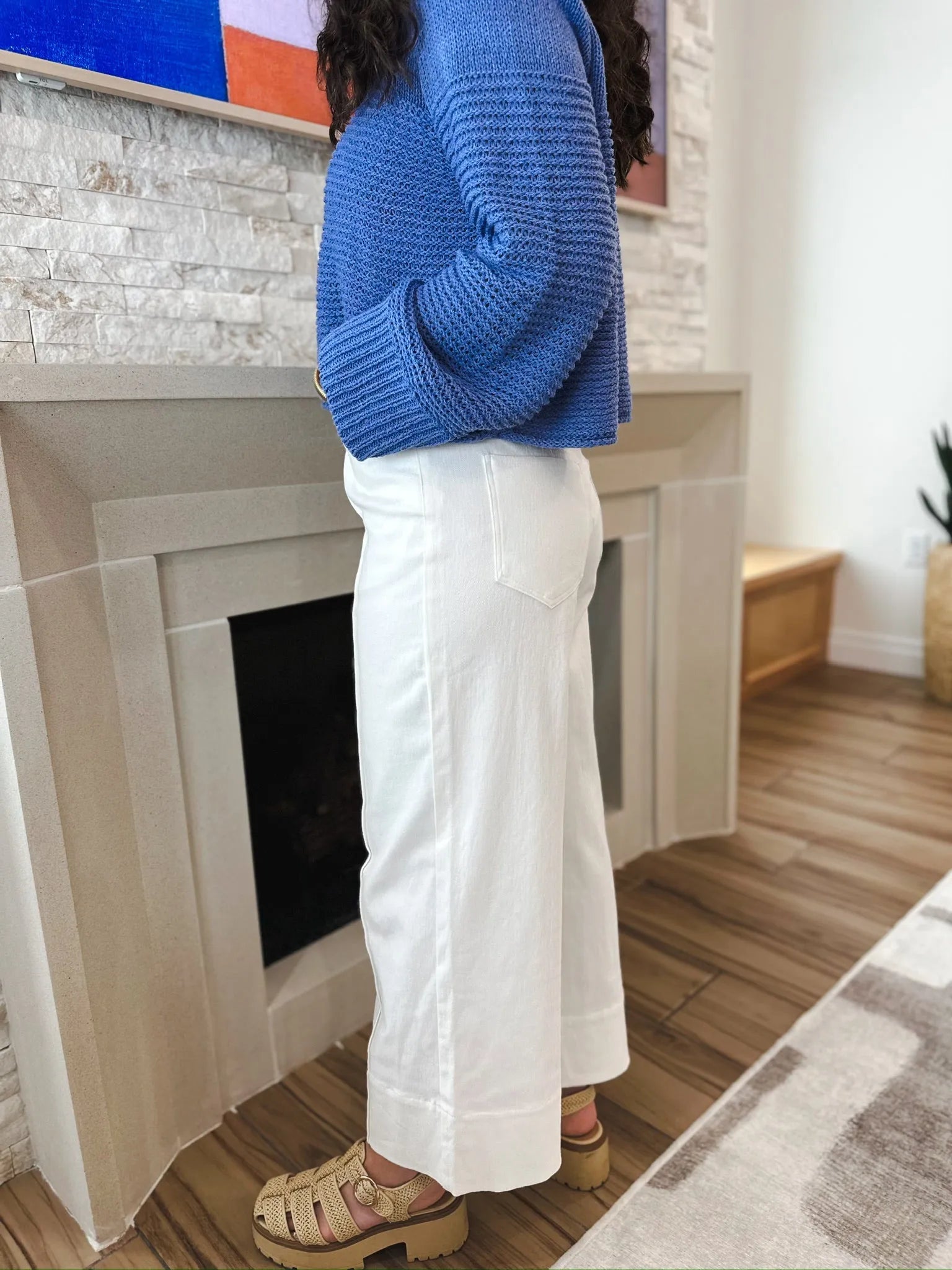 Entro white denim wide leg jeans with pleats, featuring a relaxed fit and a back pocket. Woman wearing blue sweater and tan