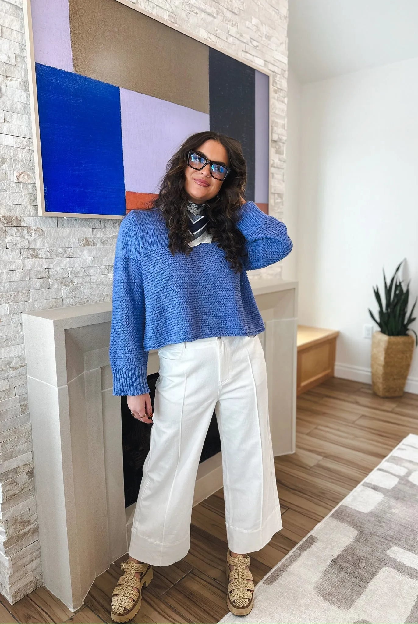 Woman wearing blue sweater and white wide-leg pleated jeans with sandals. The jeans are high-waisted and culotte-style