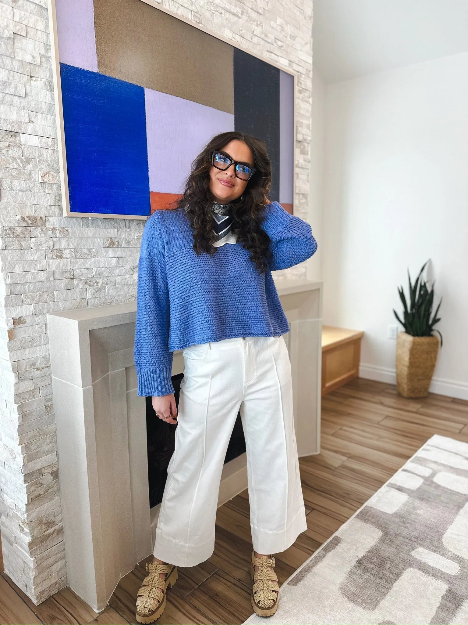Woman wearing blue sweater and white wide-leg pleated jeans with sandals. The jeans are high-waisted and culotte-style