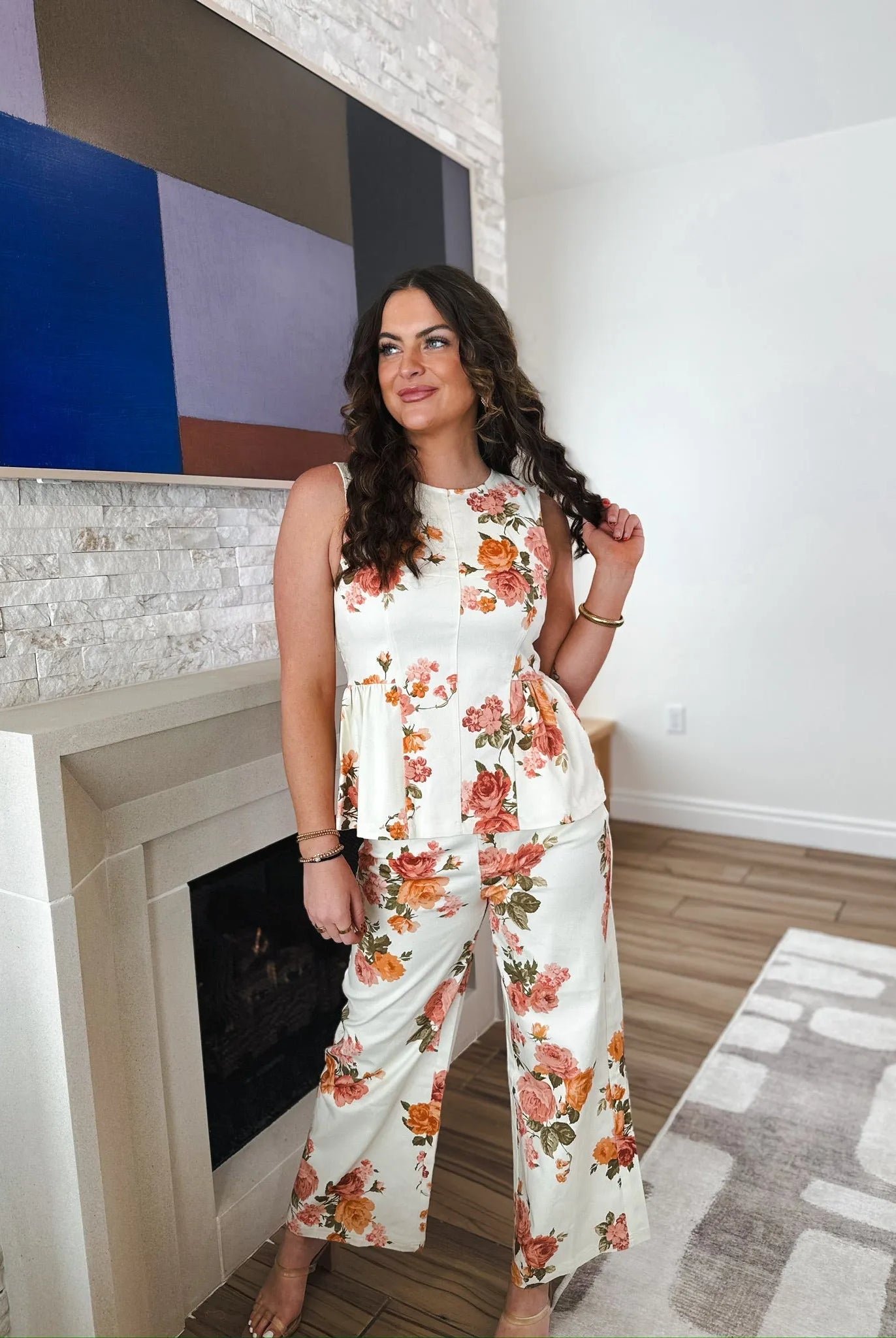Woman wearing a white floral peplum top and wide-leg pants with orange and pink roses. Entro brand.