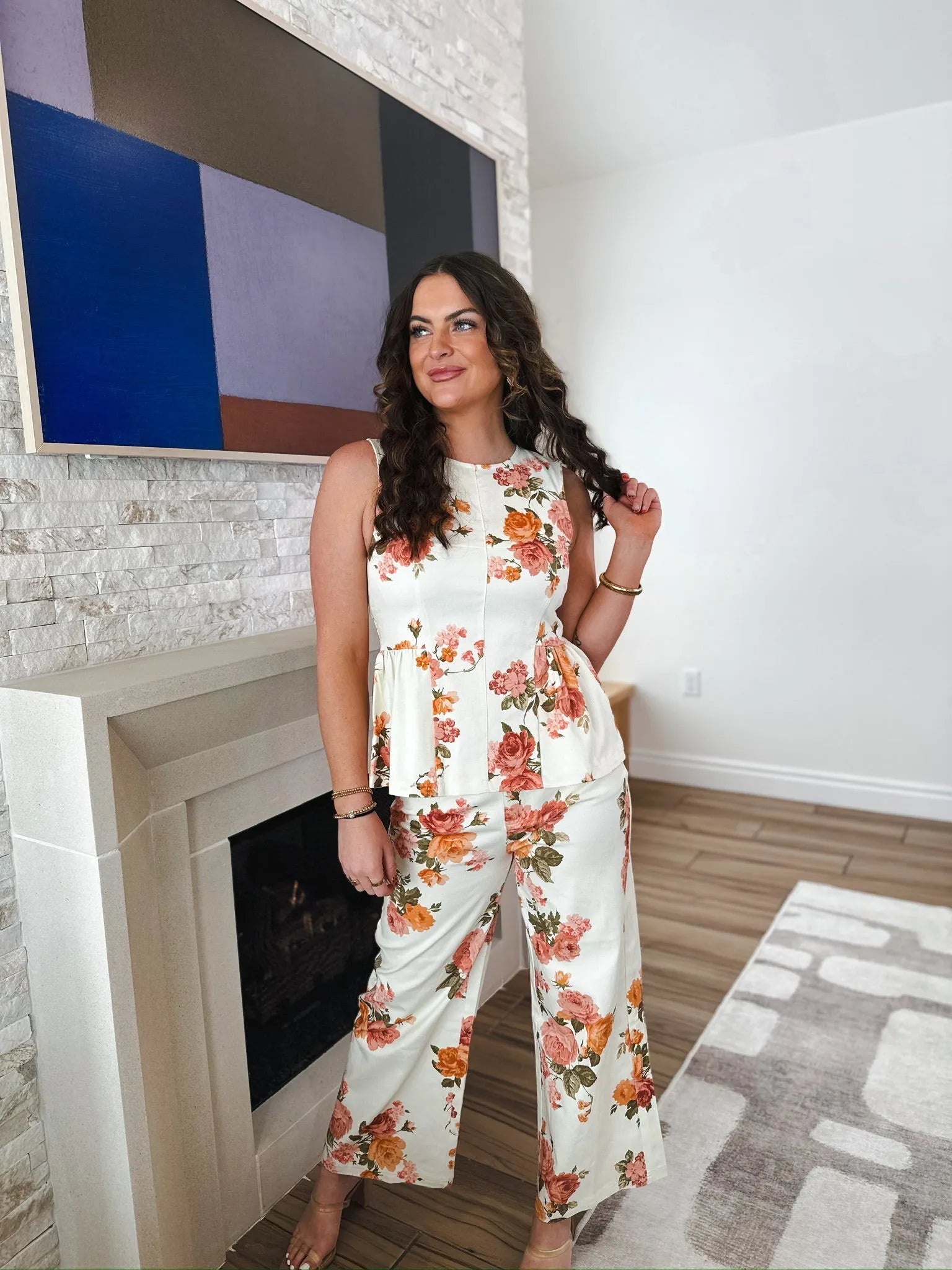 Woman wearing a white floral peplum top and wide-leg pants with orange and pink roses. Entro brand.