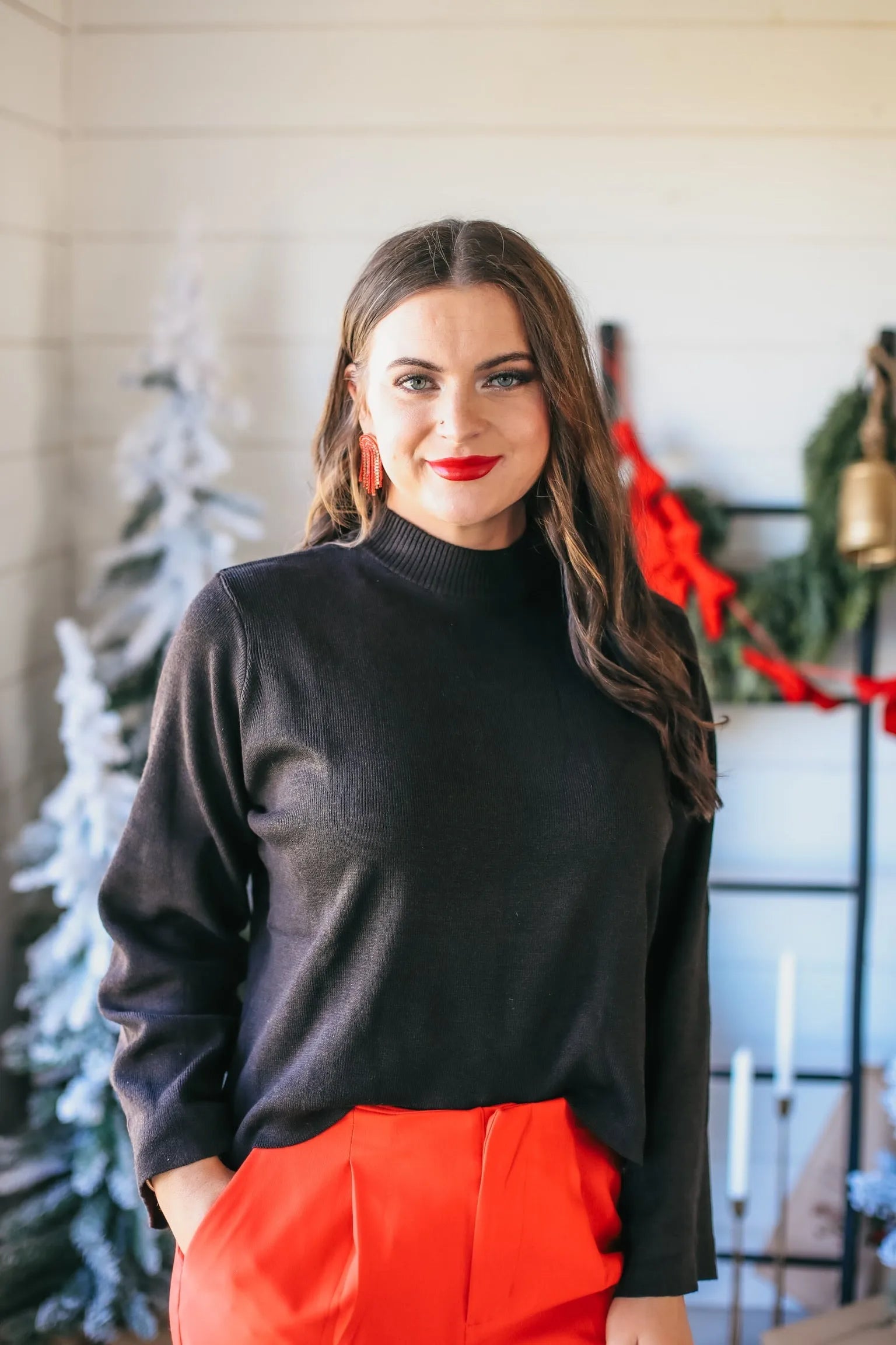 Entro wide sleeve black mock neck sweater worn by a woman with red lipstick and earrings, paired with red pants. Festive