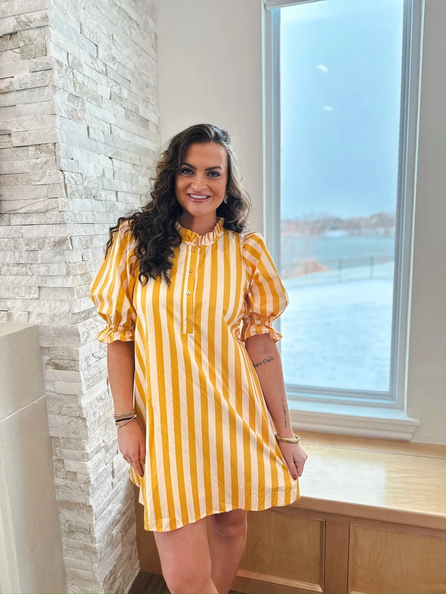Woman wearing a yellow and white striped cotton dress with a ruffle neck and puff sleeves. The dress has a button placket.