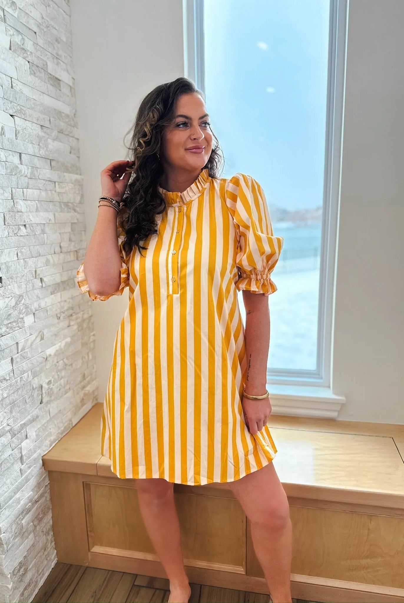 Woman wearing a yellow and white vertically striped cotton dress with a ruffle neck and short puff sleeves.