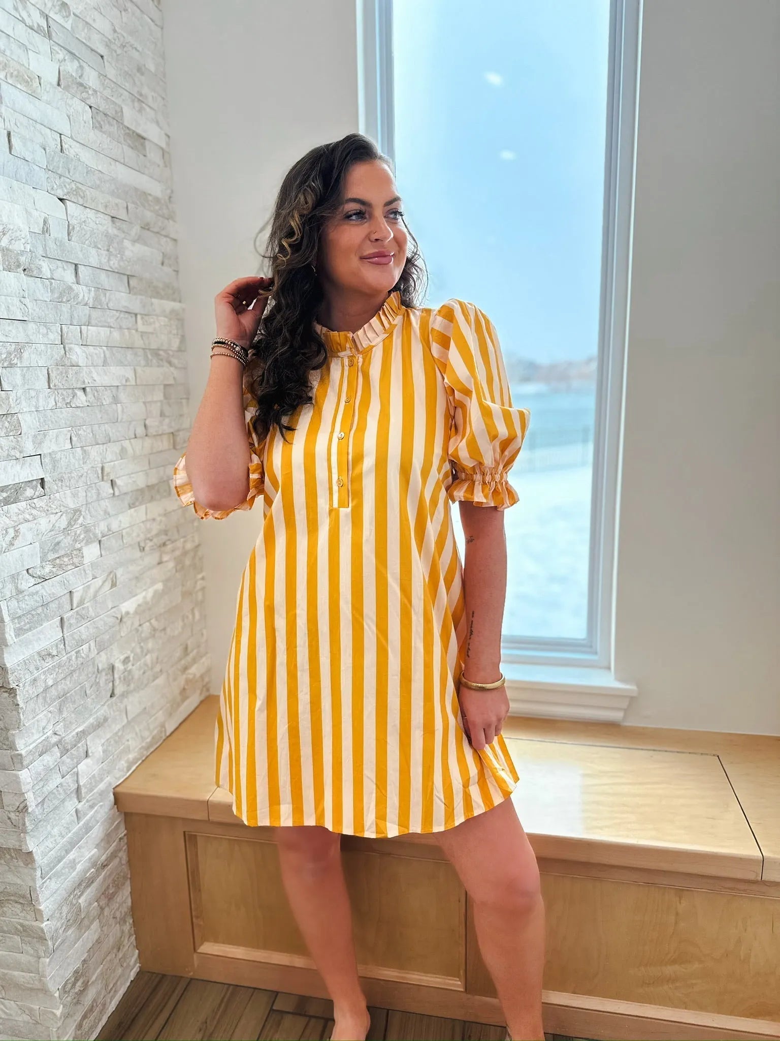 Woman wearing a yellow and white vertically striped cotton dress with a ruffle neck and short puff sleeves.