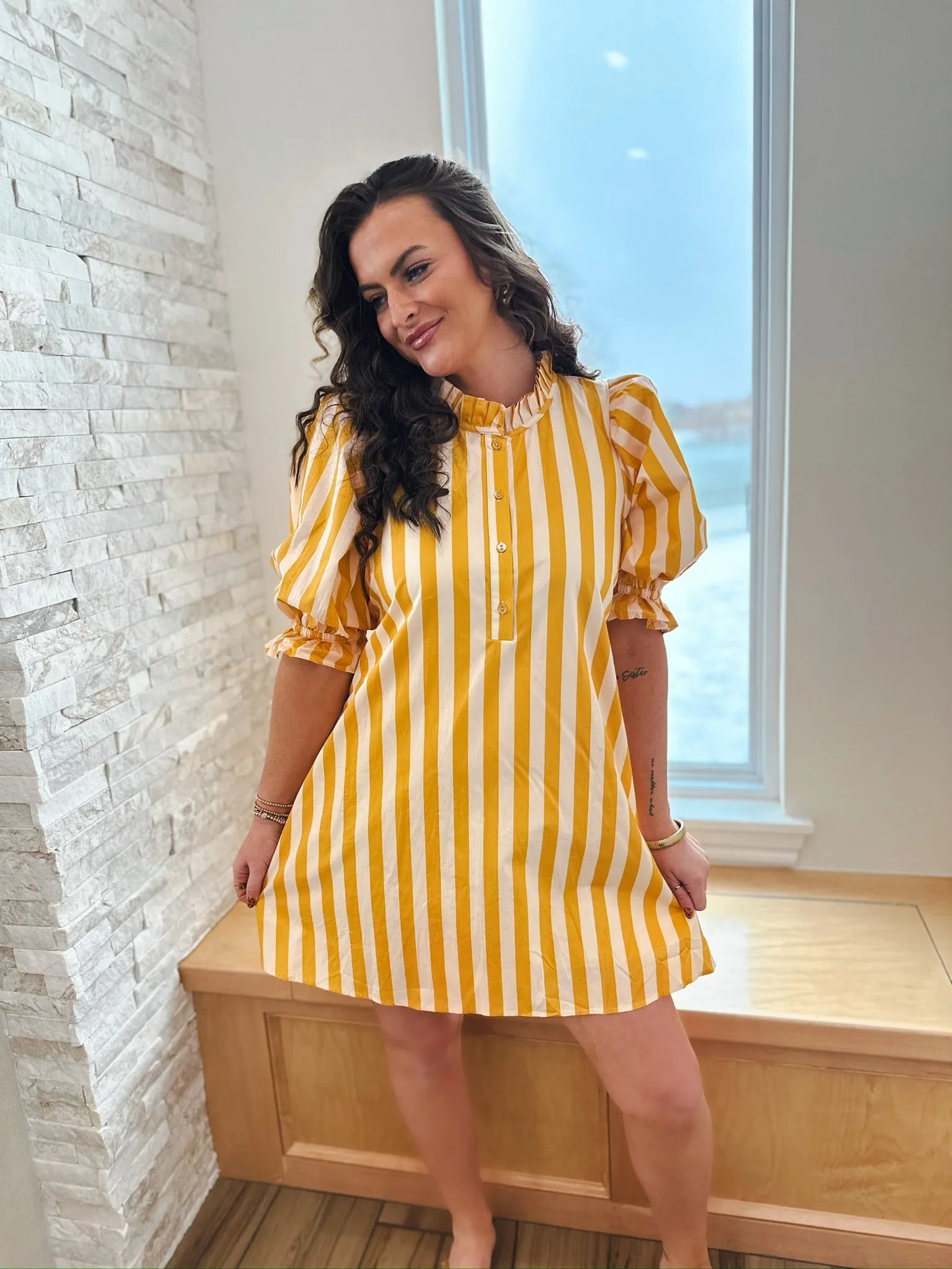 Woman wearing a yellow and white striped cotton dress with a ruffle neck and puff sleeves.