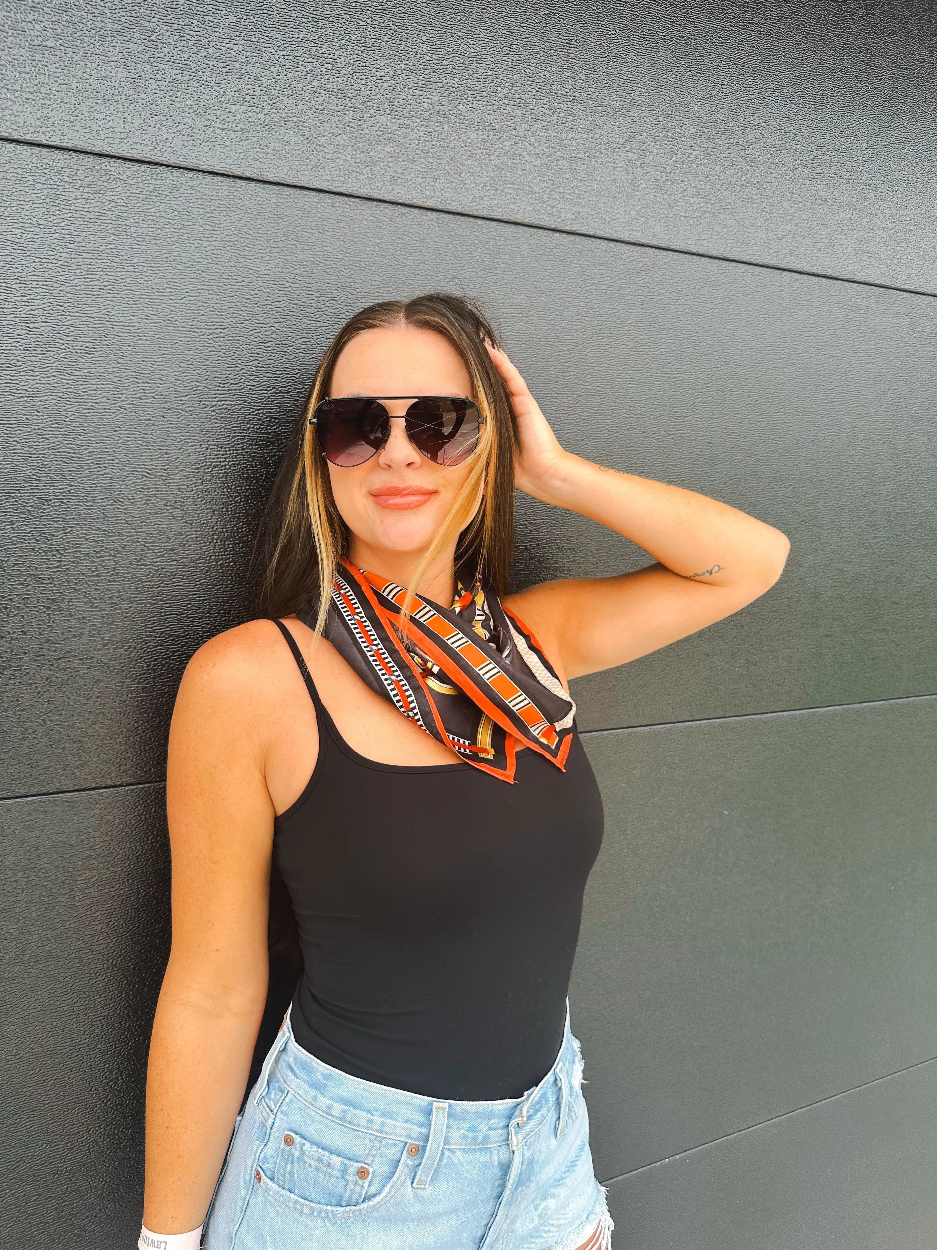 Woman wearing black tank top and denim shorts, accessorized with a silk-texture square scarf featuring an equestrian print