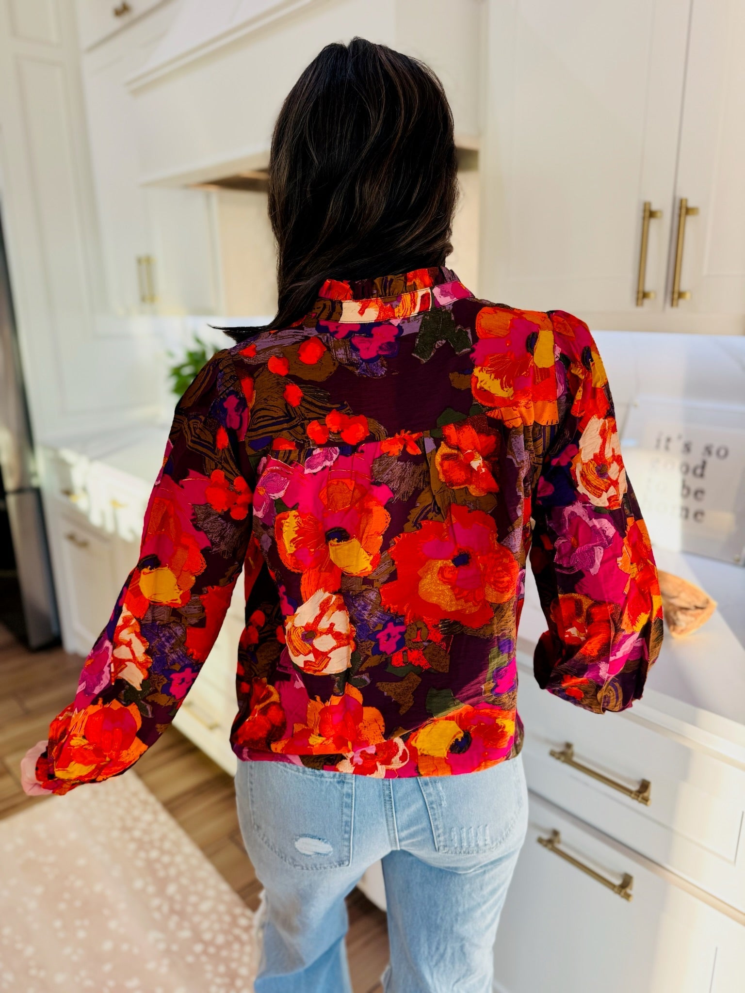 Back view of a woman wearing a Fate multi-color floral print blouse with ruffled V-neck and long sleeves, paired with light
