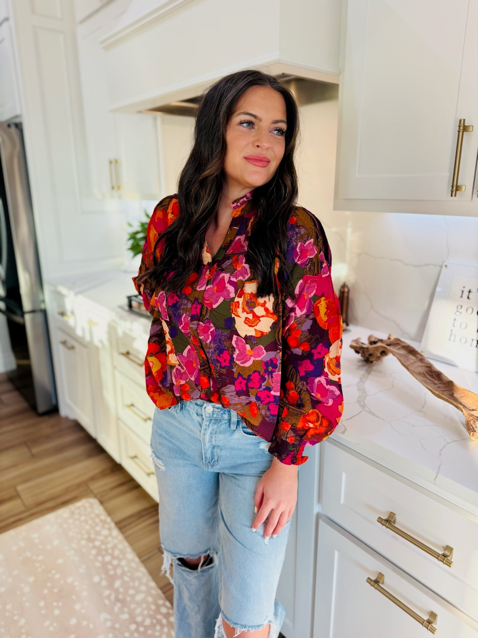 Model wearing a multi-color floral print blouse with ruffled V-neck and light wash ripped jeans.