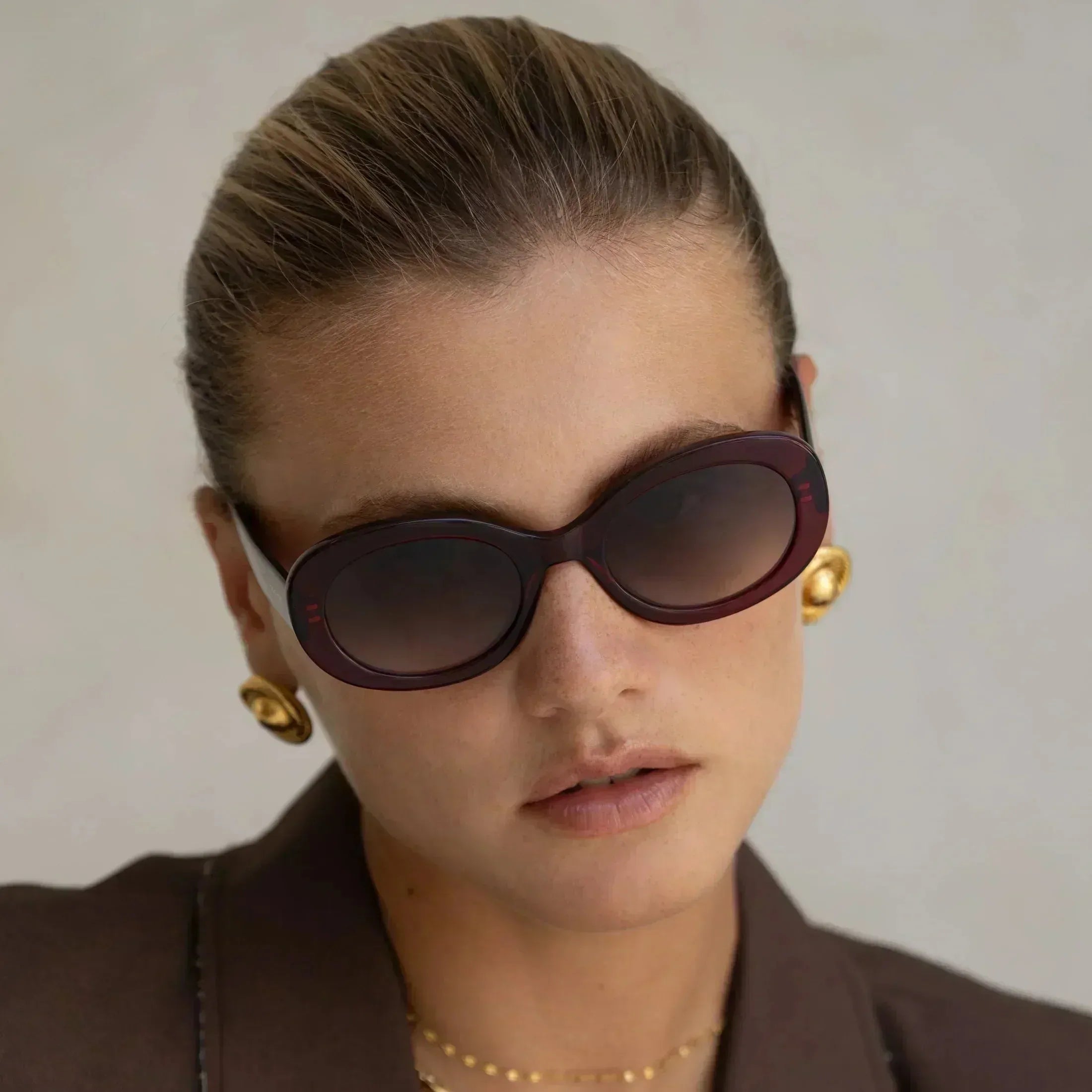 Freyrs Aria women's classic oval burgundy acetate sunglasses with gradient lenses and gold statement earrings.