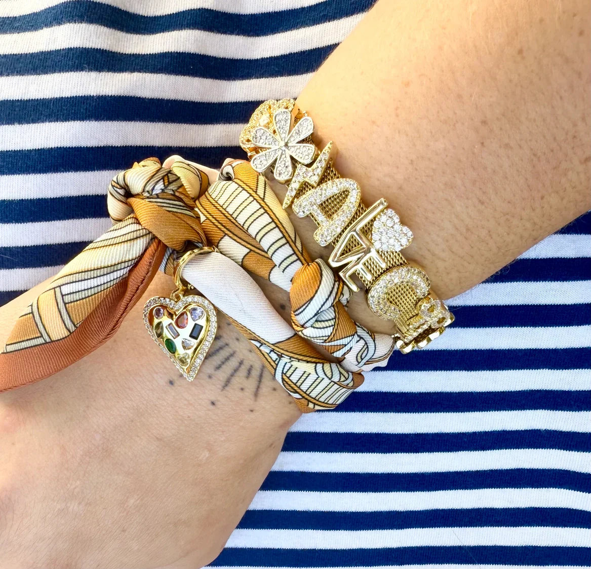Gold plated slider charms including "LOVE" letters with CZs, a heart with colorful gemstones, and a flower charm, on a