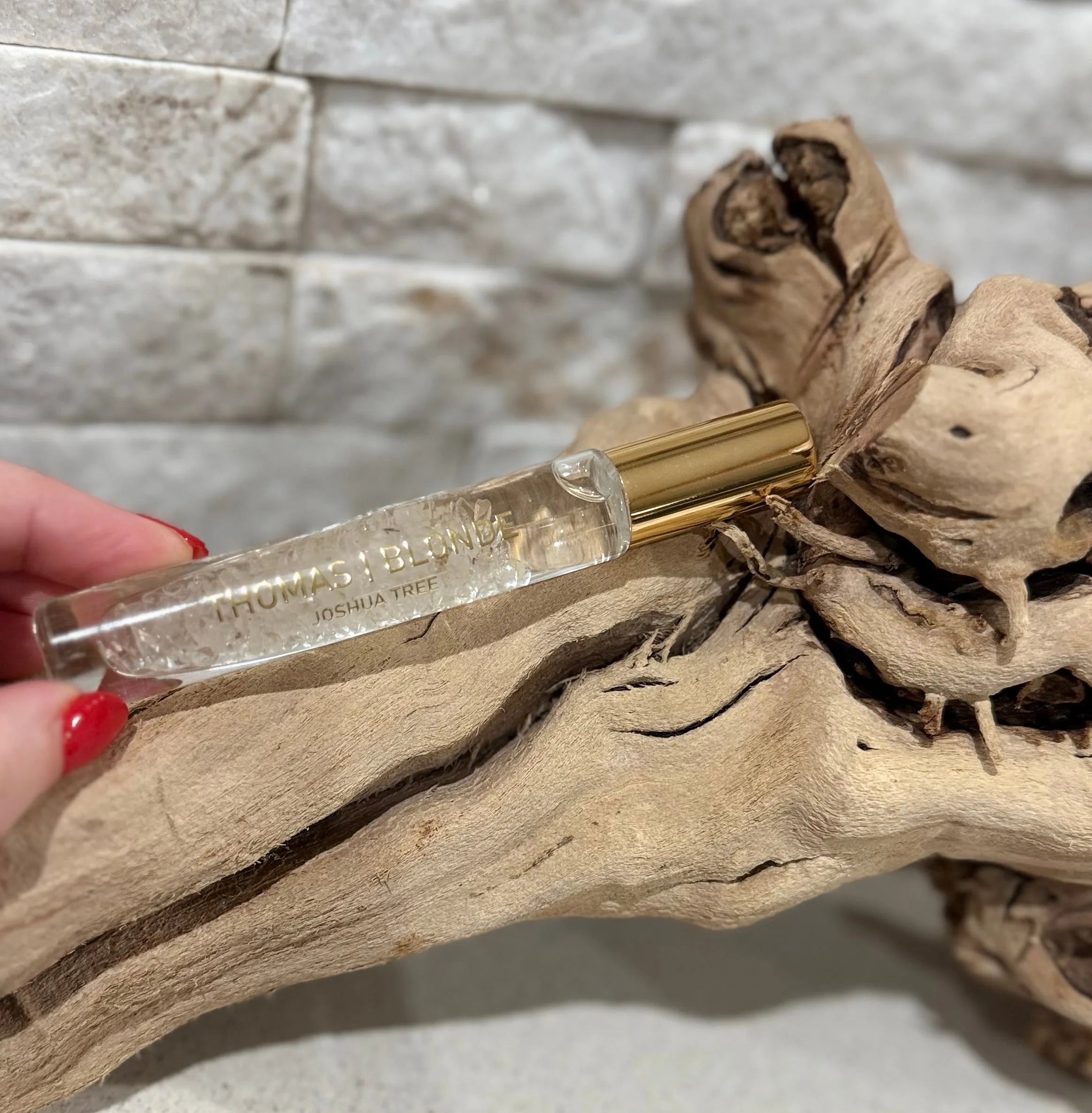 Thomas Blonde Joshua Tree perfume roller with clear liquid and botanical inclusions, gold cap, held by hand with red nail