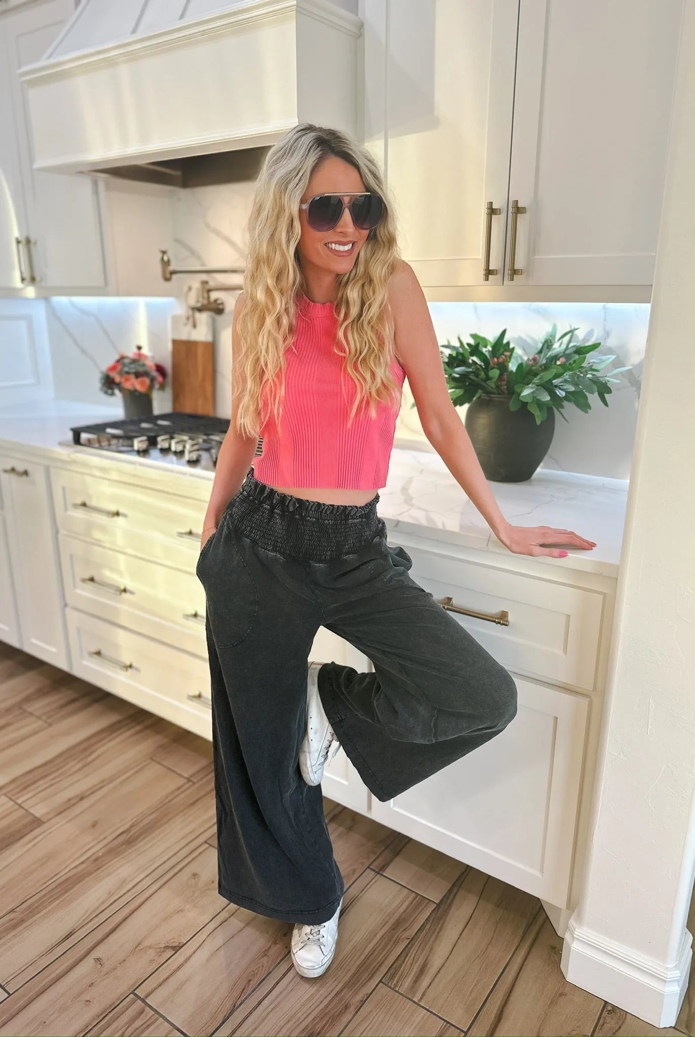 Woman wearing HyFVE black wash elastic waist wide-leg trousers and a pink crop top, leaning on a kitchen counter.