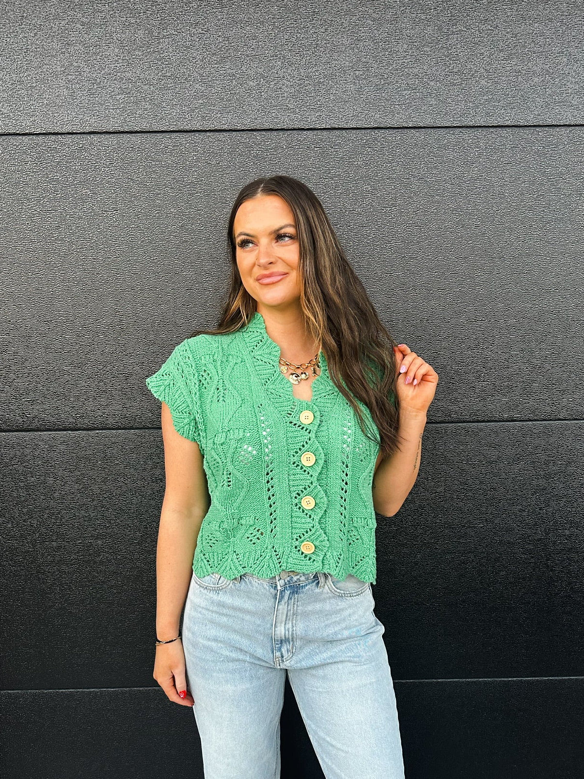Green short-sleeve knitted button-down sweater with intricate openwork patterns and light wood buttons. Model wears light