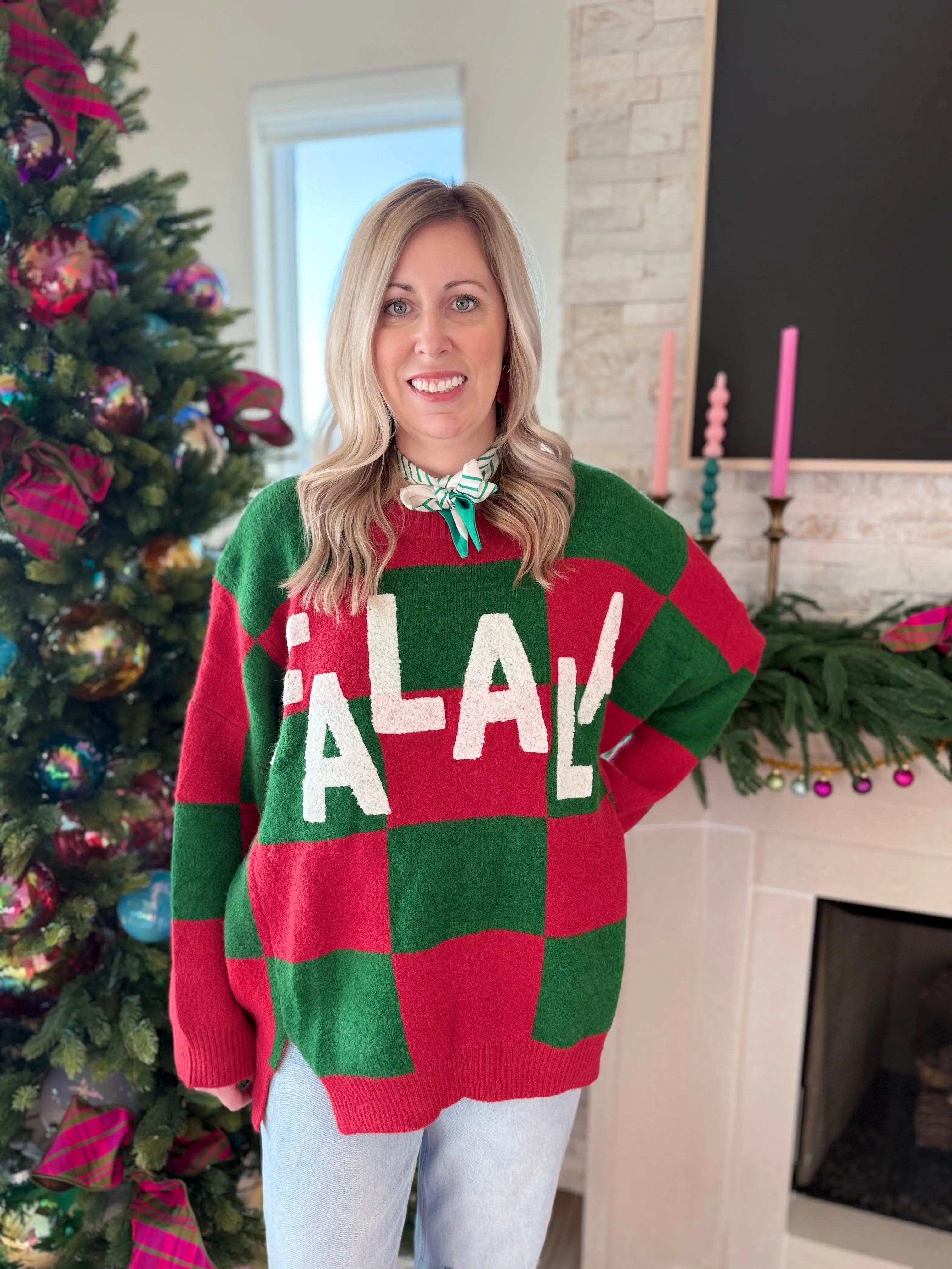 Woman wearing a red and green checkered holiday sweater with 'FA LA LA' text. She has blonde hair and is smiling, with a