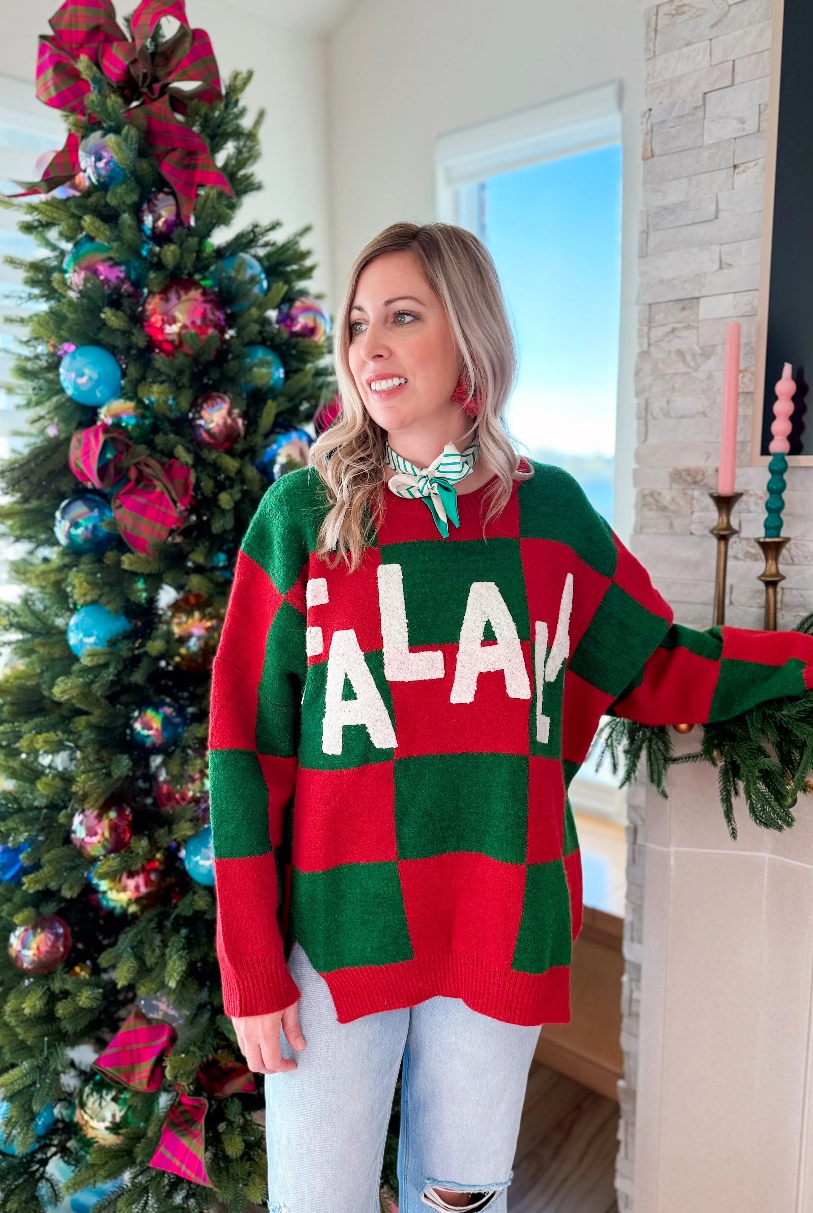 Woman wearing a red and green checkered holiday sweater with 'Fa-La-La' text. Christmas tree in background.