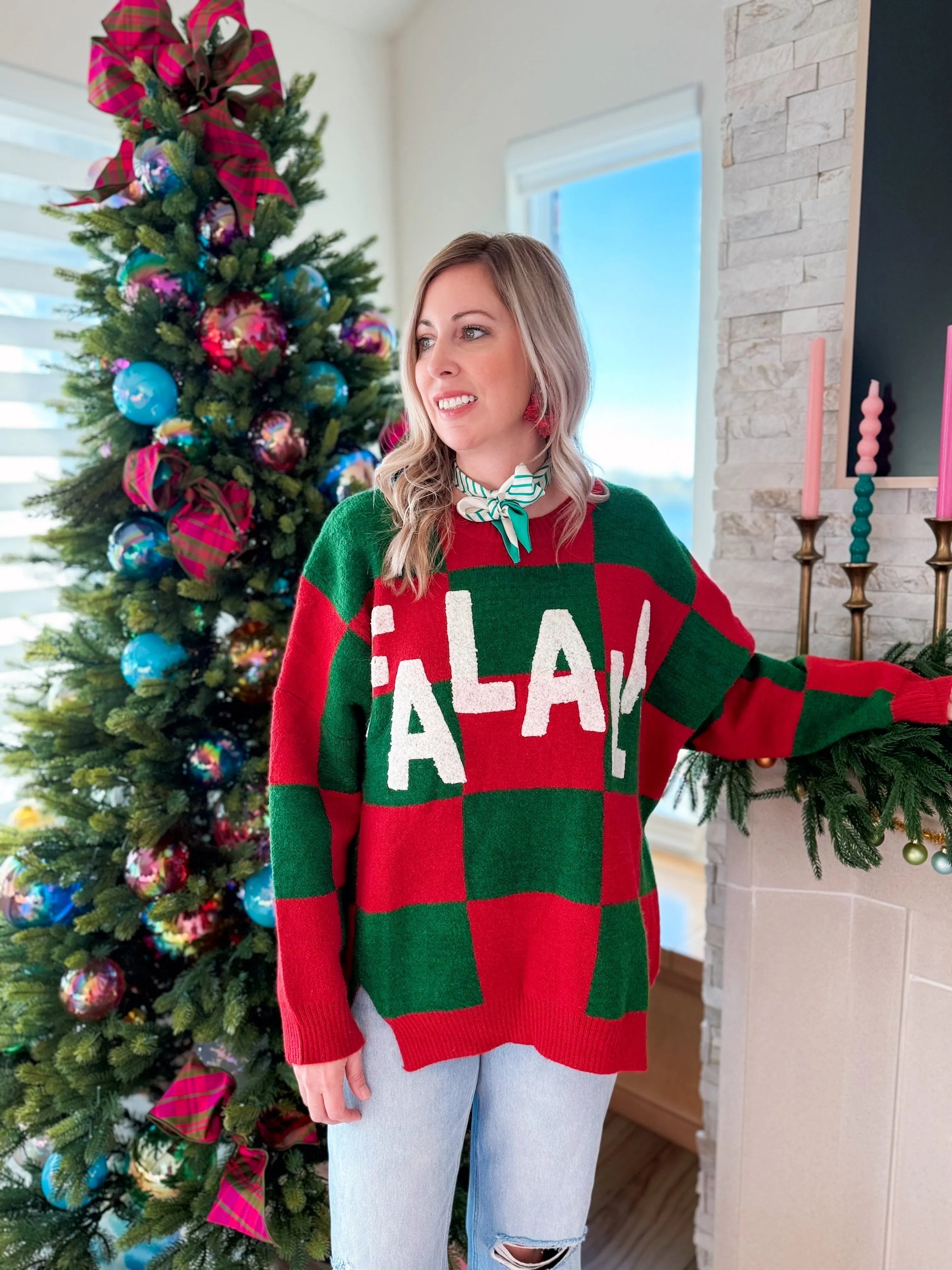 Woman wearing a red and green checkered holiday sweater with 'Fa-La-La' text. Christmas tree in background.