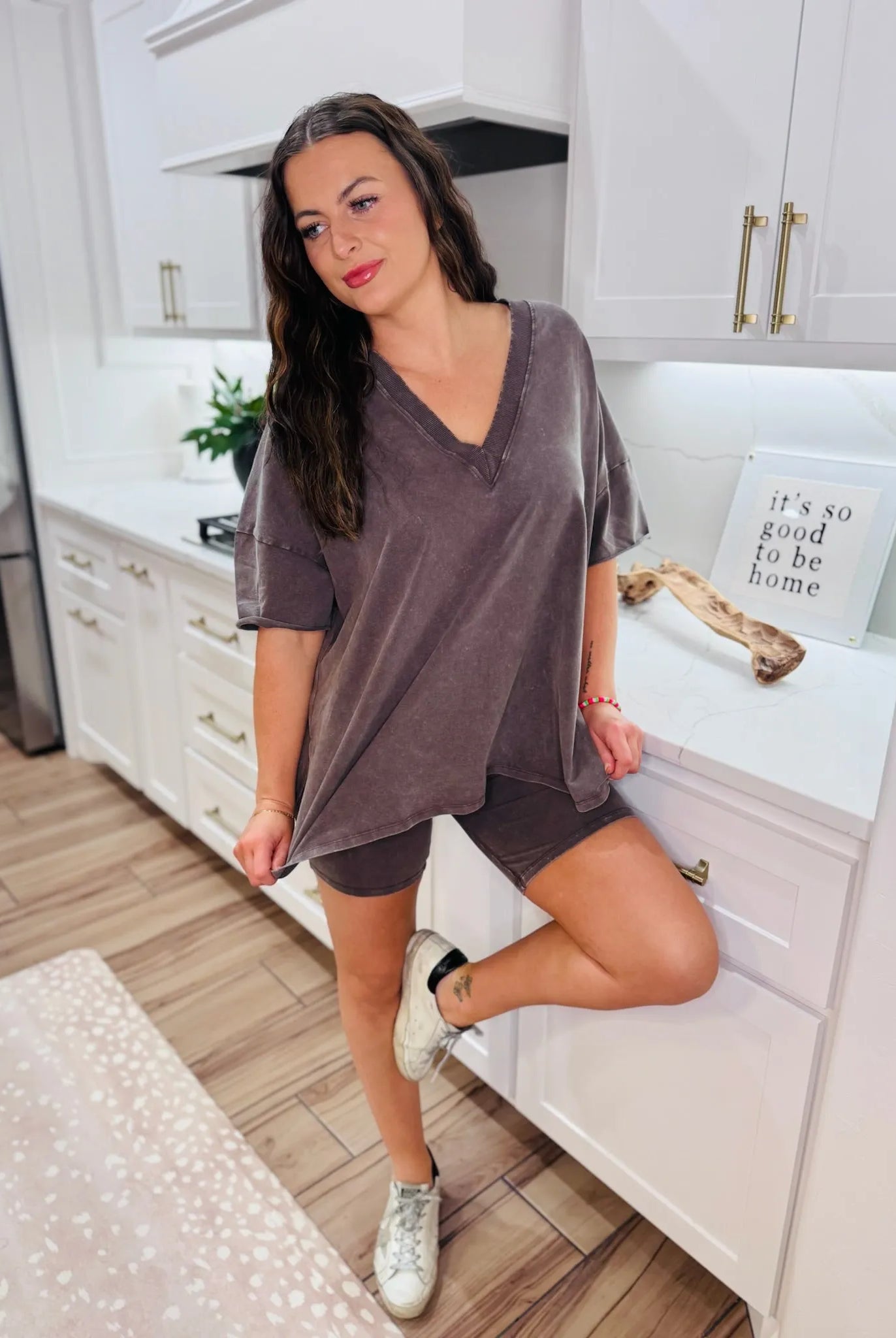 Woman wearing a chocolate brown boxy V-neck t-shirt and matching shorts set, standing in a kitchen.