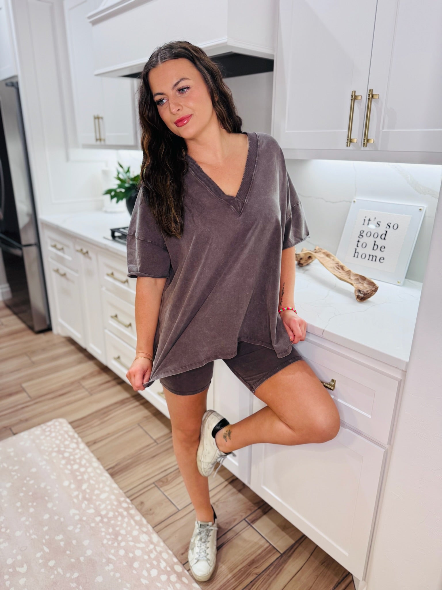 Woman wearing a chocolate brown boxy V-neck t-shirt and matching shorts set, standing in a kitchen.