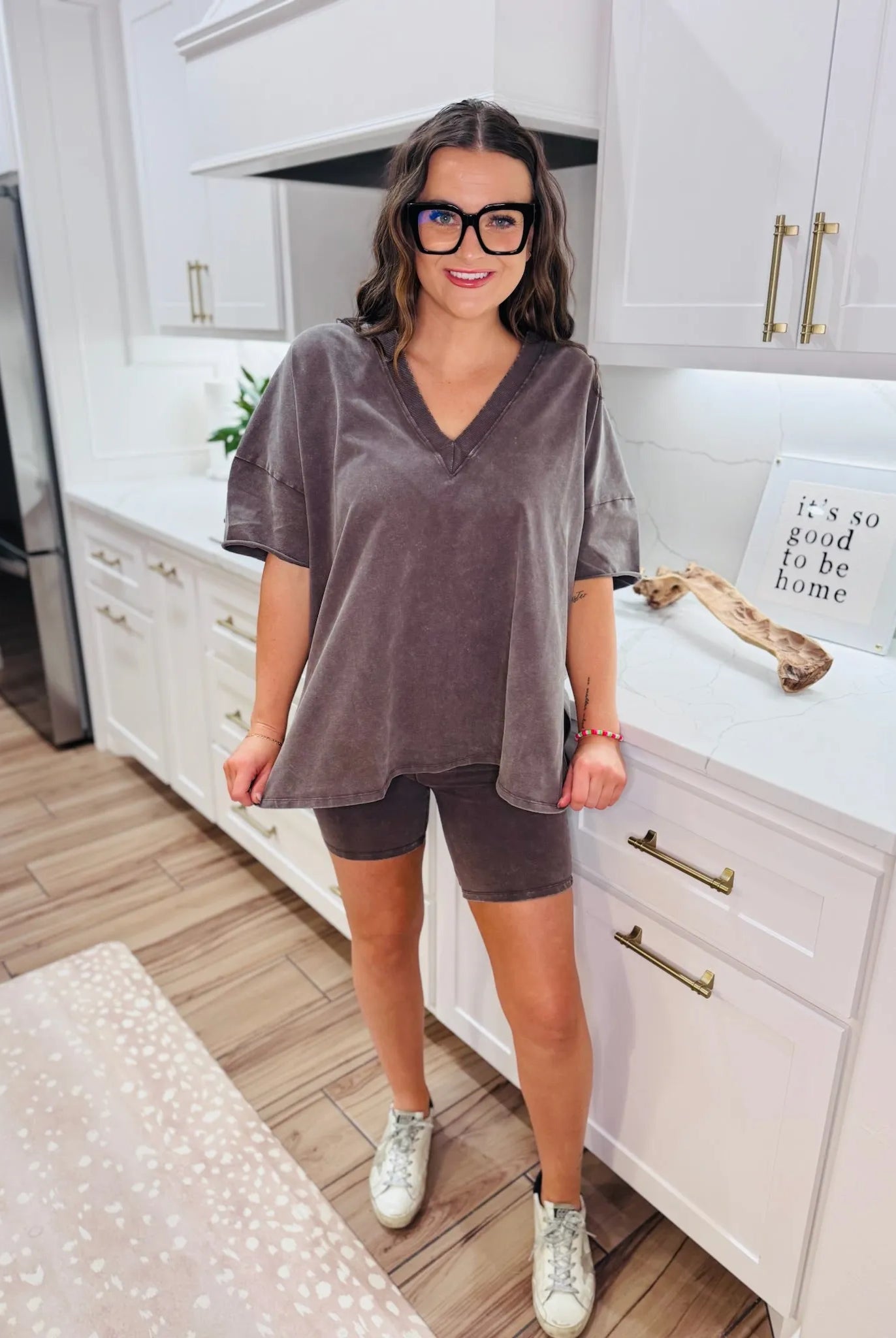 Woman wearing a chocolate brown boxy V-neck t-shirt and matching biker shorts, paired with white sneakers and black glasses.