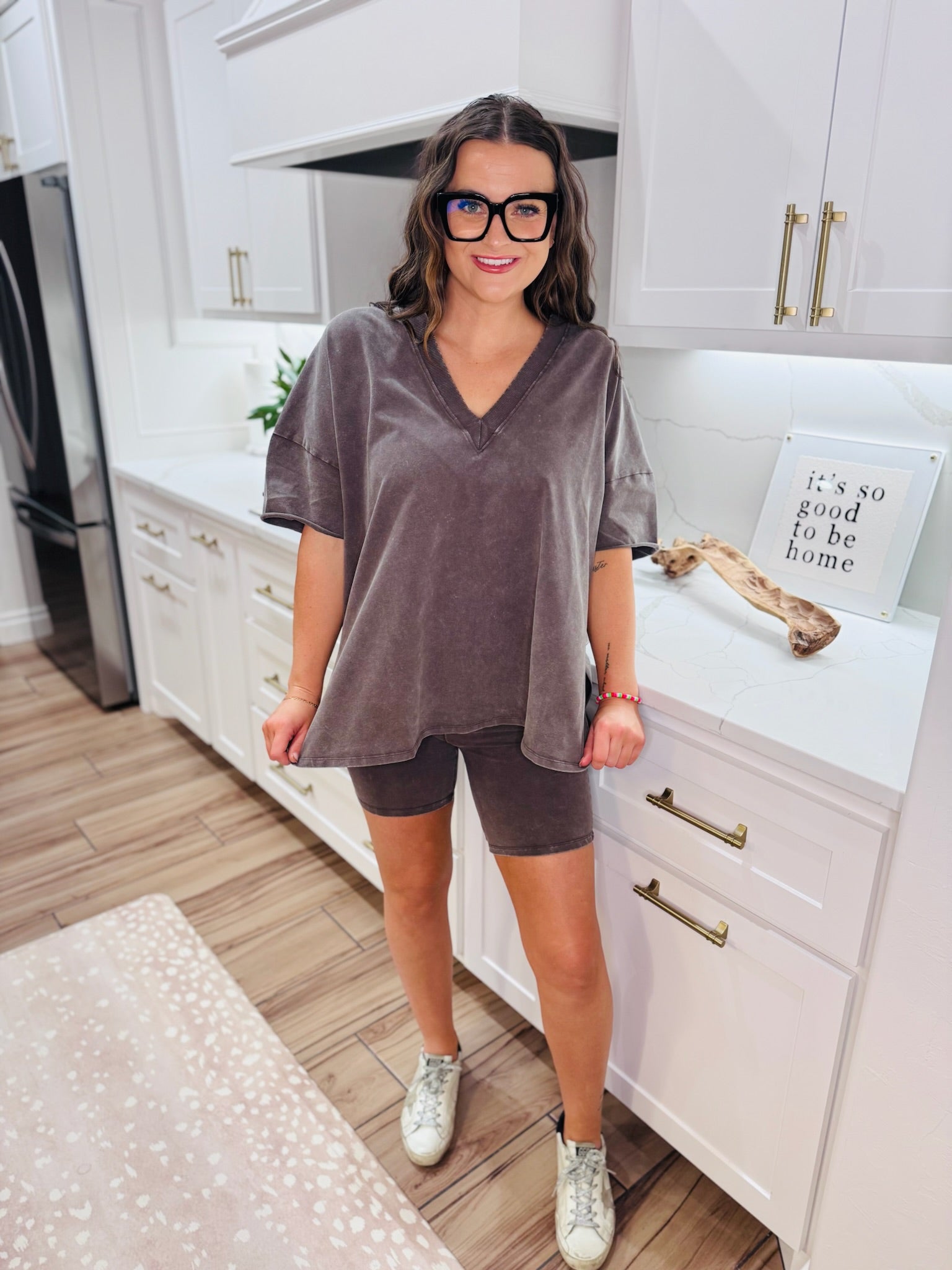 Woman wearing a chocolate brown boxy V-neck t-shirt and matching biker shorts, paired with white sneakers and black glasses.