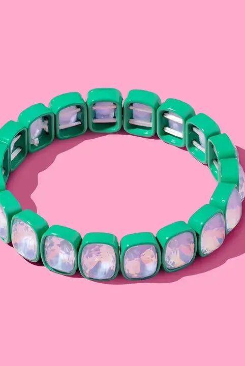 A Layla Enamel & Stone Stacking Bracelet with square green enamel beads and clear, iridescent stones on a pink background.