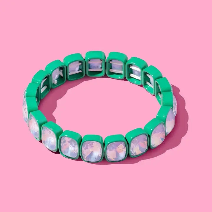 A Layla Enamel & Stone Stacking Bracelet with square green enamel beads and clear, iridescent stones on a pink background.