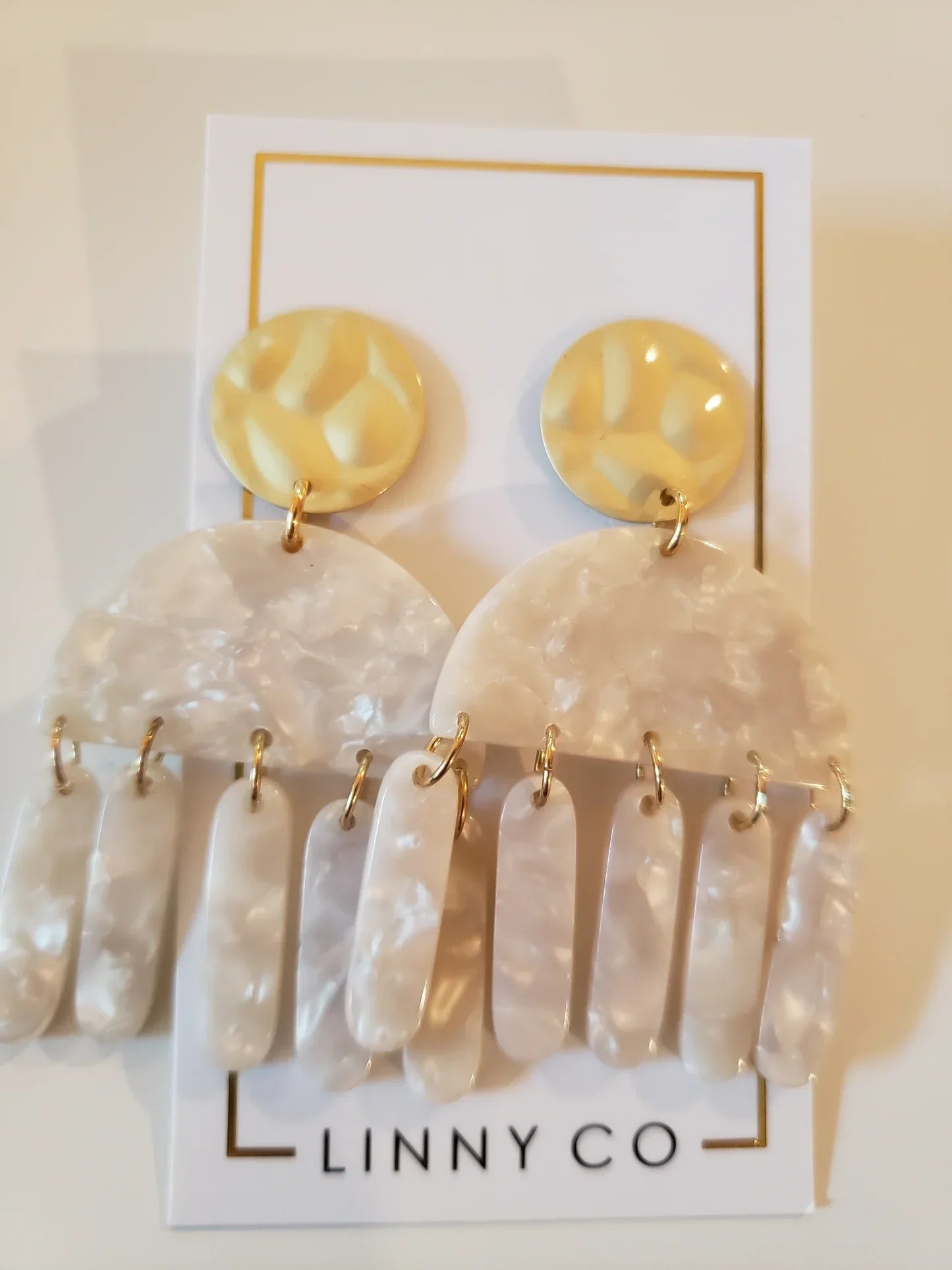 LINNY CO sensitive earrings: gold discs, white marble half-circles, and dangling white oval beads.