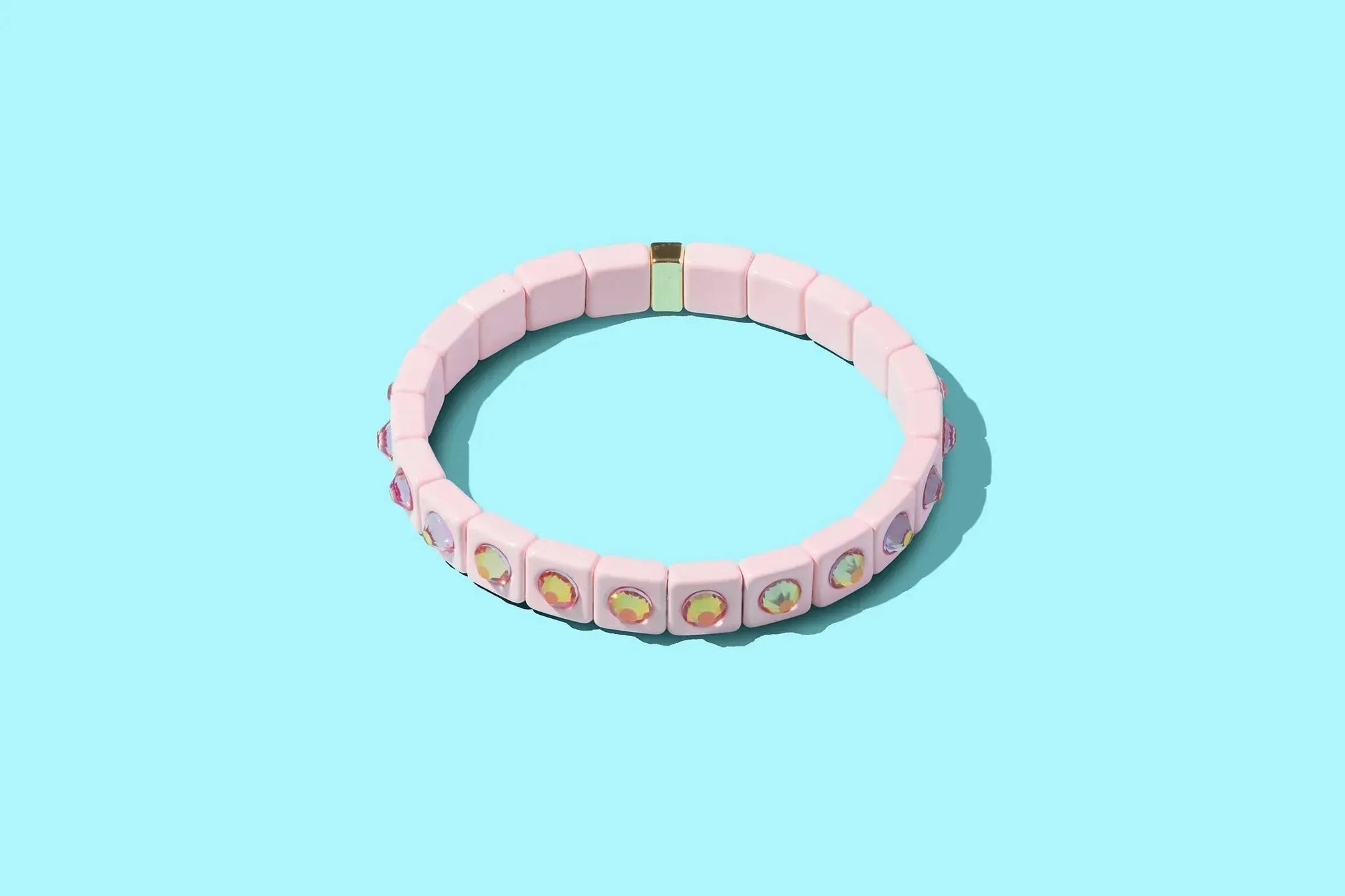 Pink enamel bracelet with square beads and iridescent stone accents on a blue background.