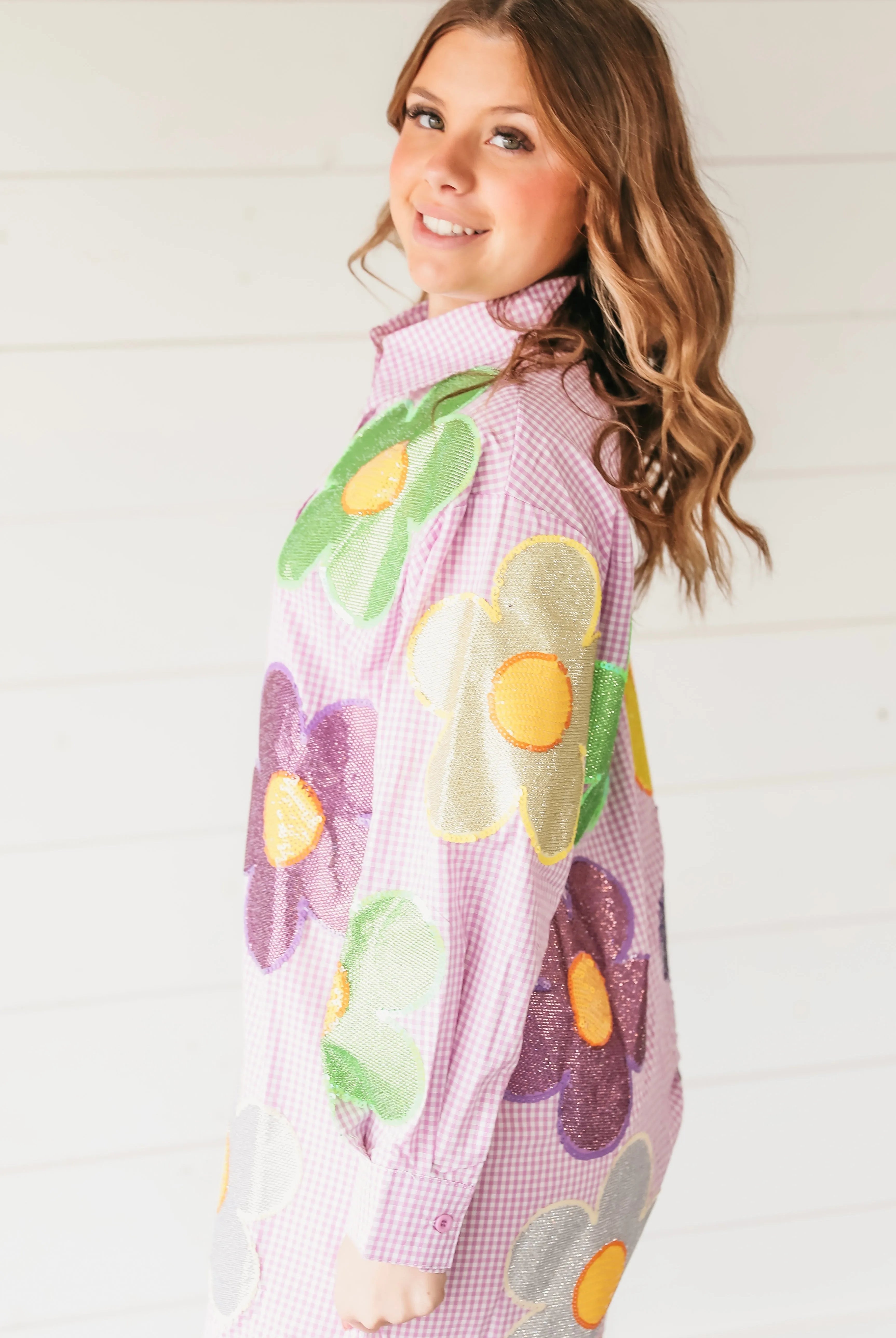 Woman wearing a pink gingham button-up romper adorned with large, colorful sequined flowers in green, purple, gold, and