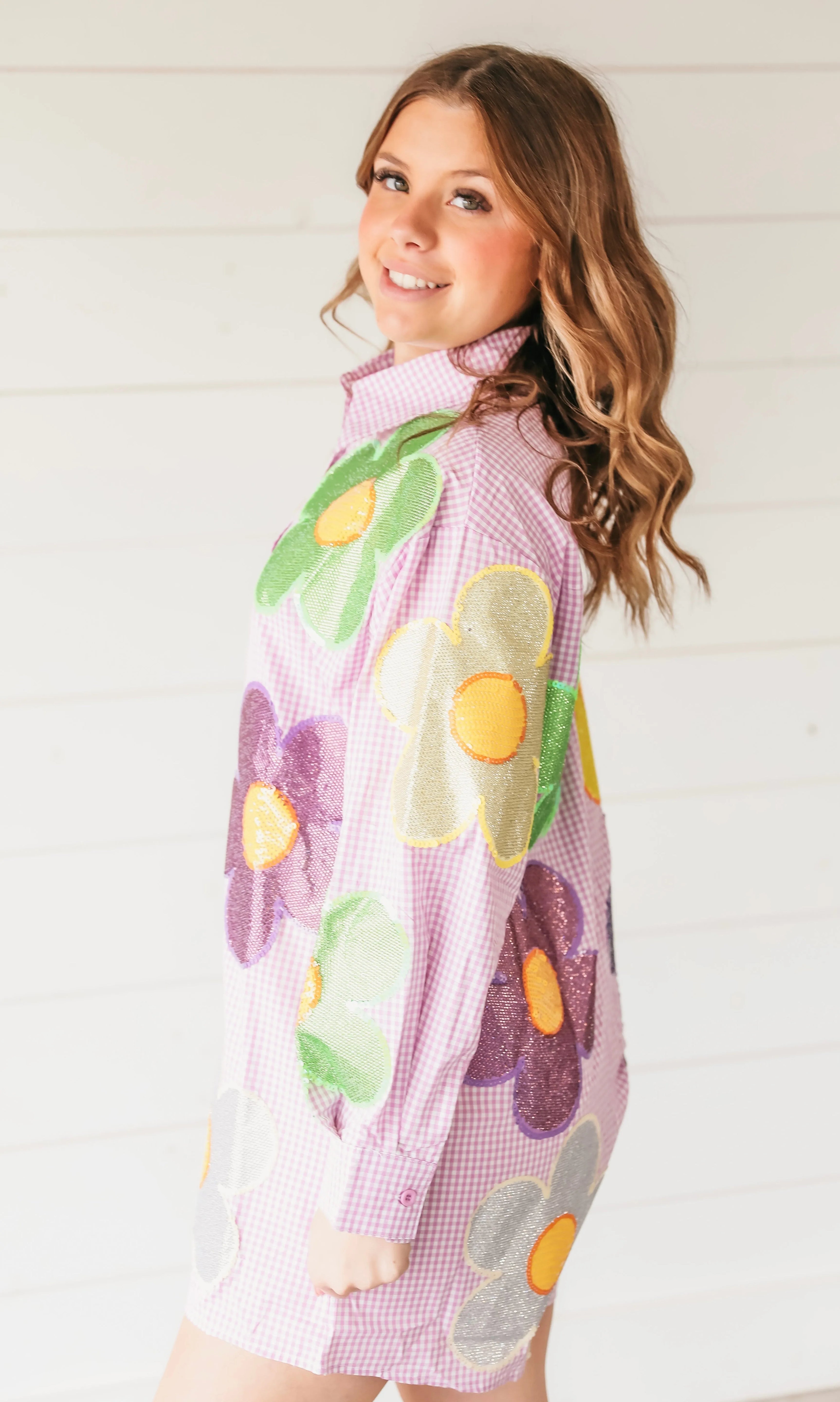 Woman wearing a pink gingham button-up romper adorned with large, colorful sequined flowers in green, purple, gold, and