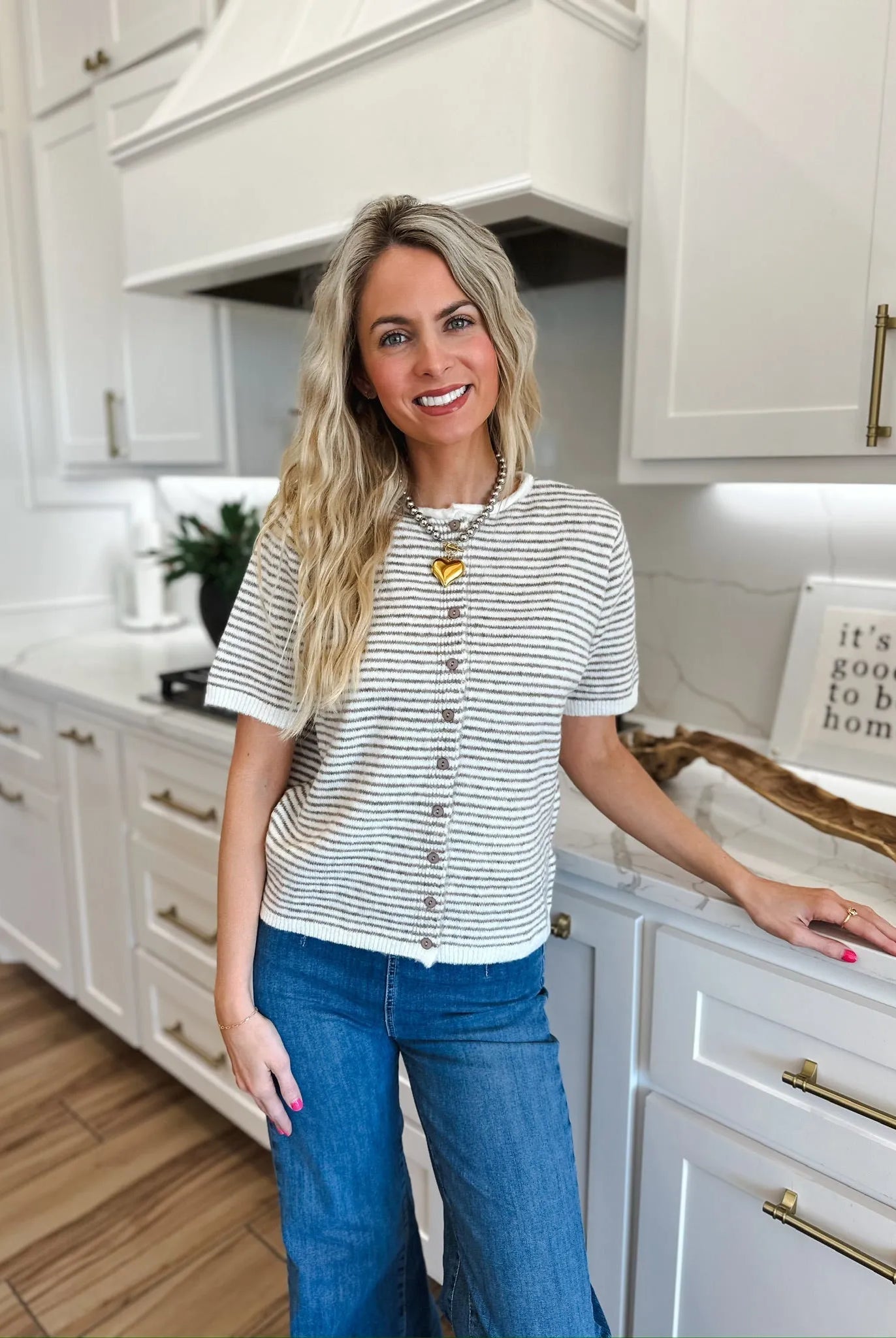 Woman wearing a cream and gray striped knit button-down short-sleeve top with blue wide-leg jeans and a heart pendant