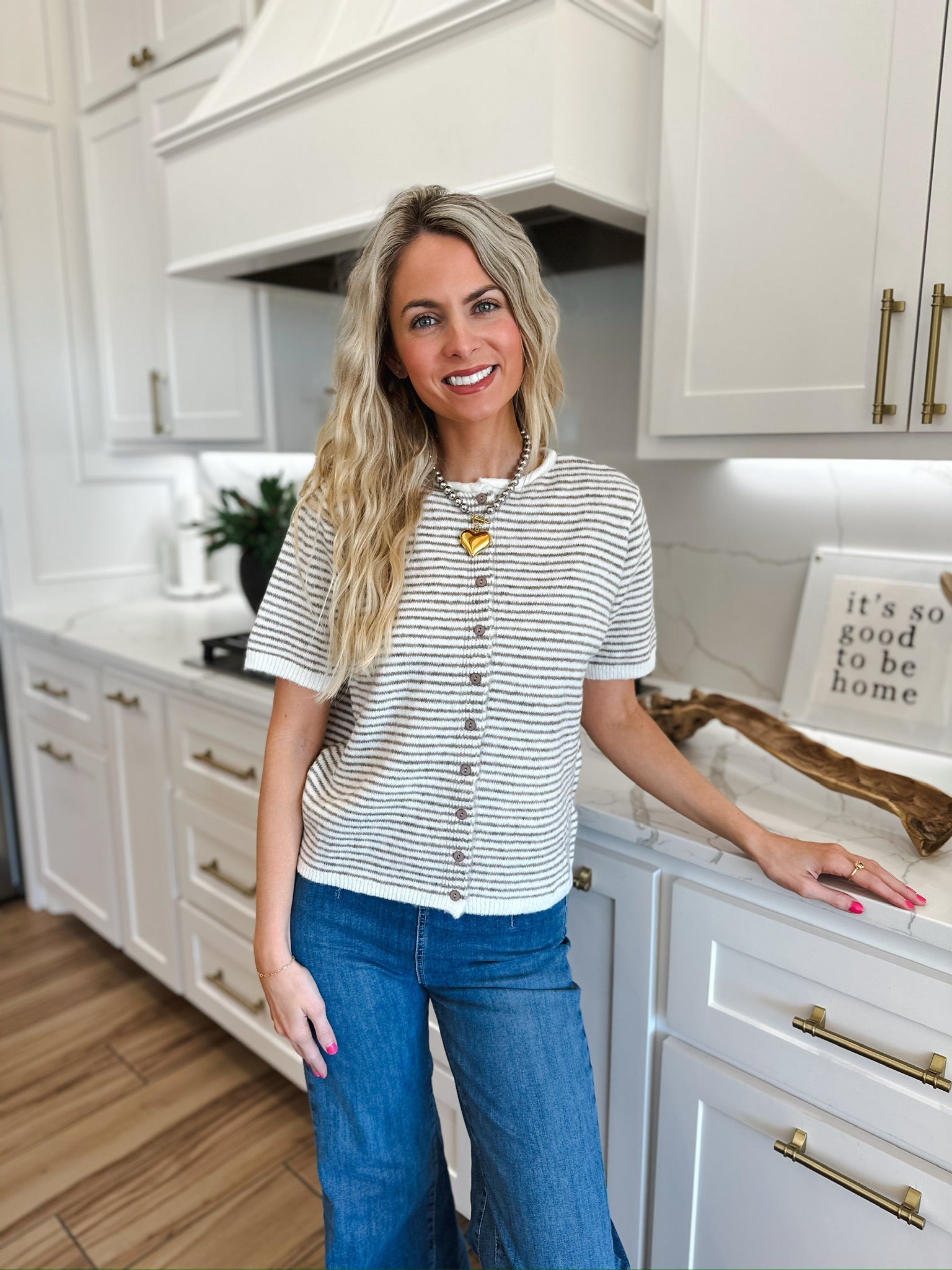 Woman wearing a cream and gray striped knit button-down short-sleeve top with blue wide-leg jeans and a heart pendant
