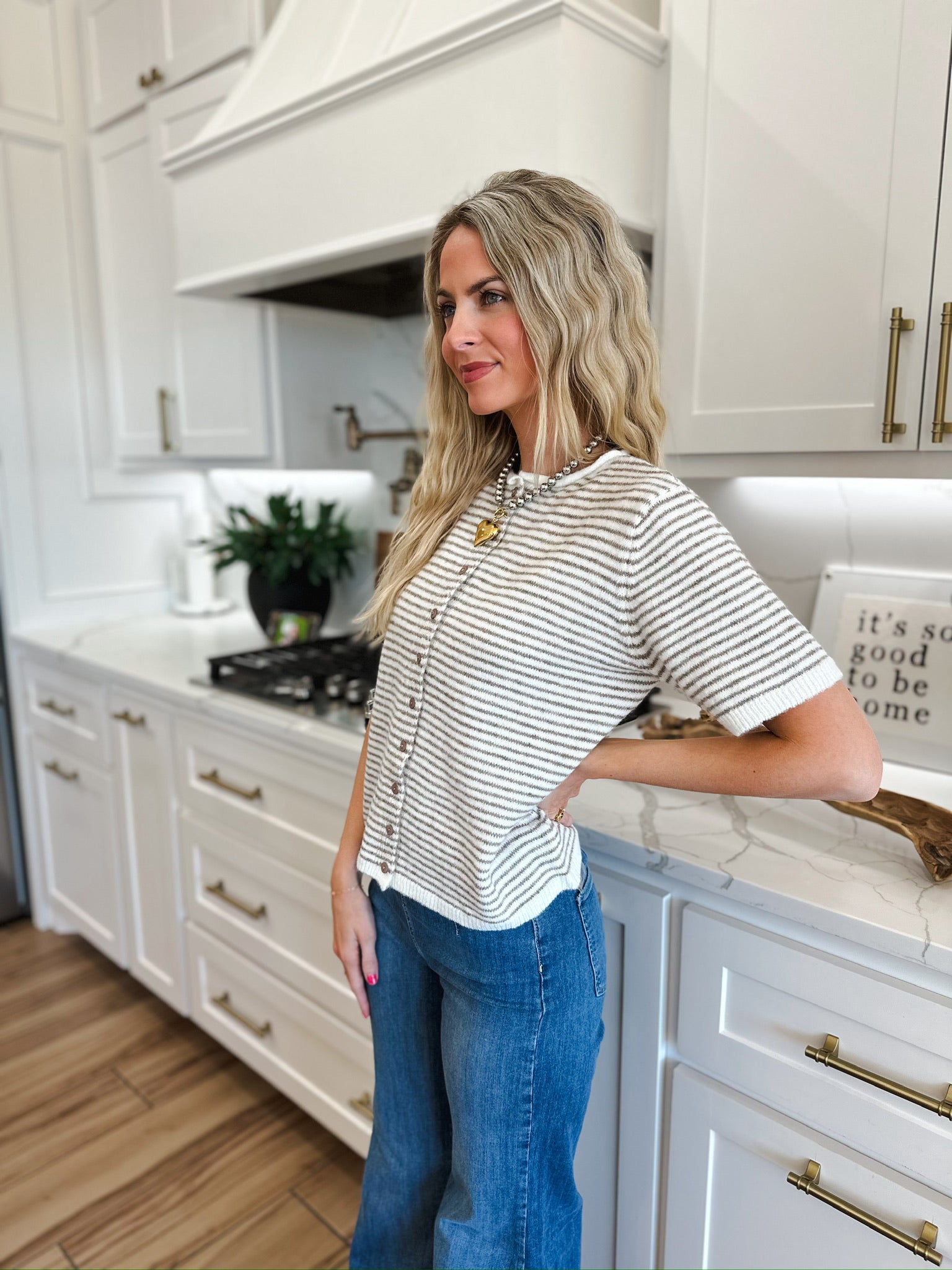 Woman wearing a cream and tan striped knit button-down top with short sleeves and a collared neckline, paired with blue