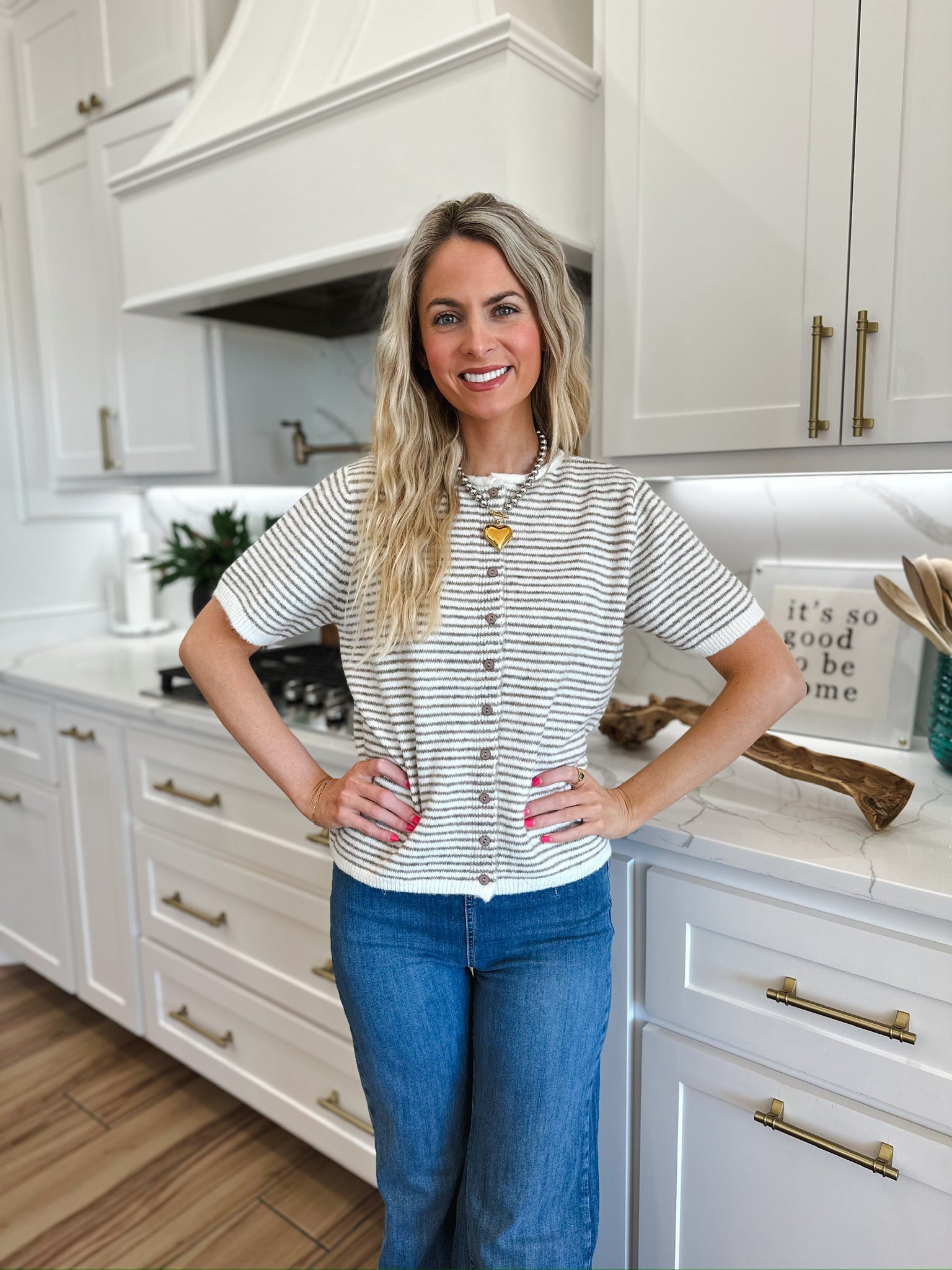 Woman wearing a cream and tan striped knit button-down short-sleeve top with blue jeans and a heart pendant necklace.