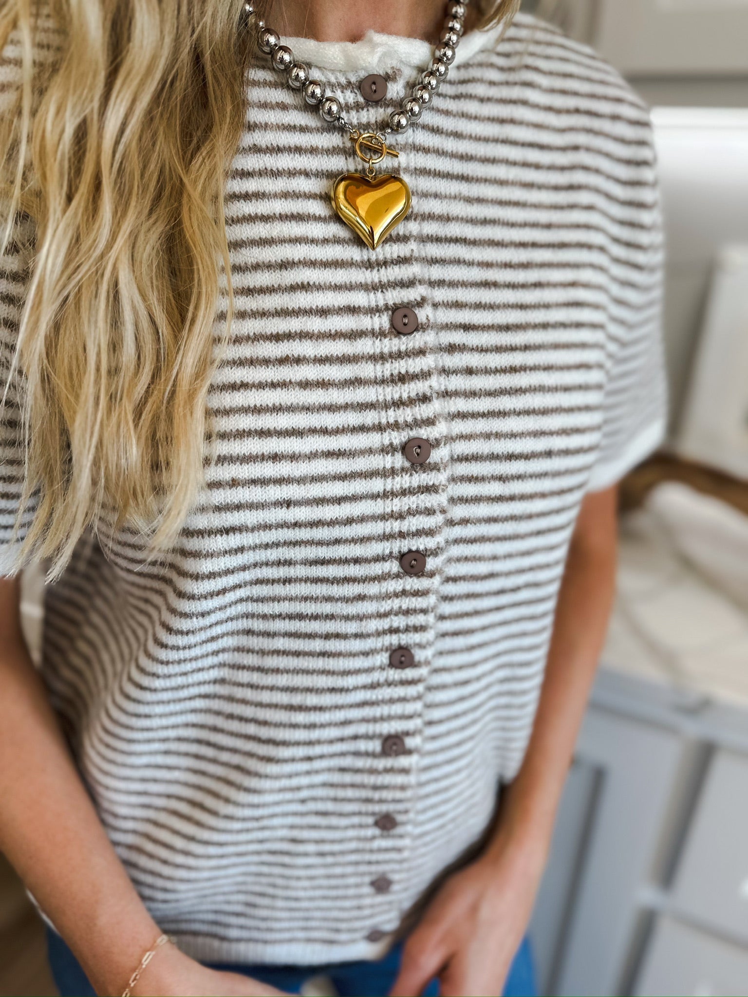 Cream and brown striped knit button-down top with short sleeves. Features a white ribbed neckline and brown buttons. A gold