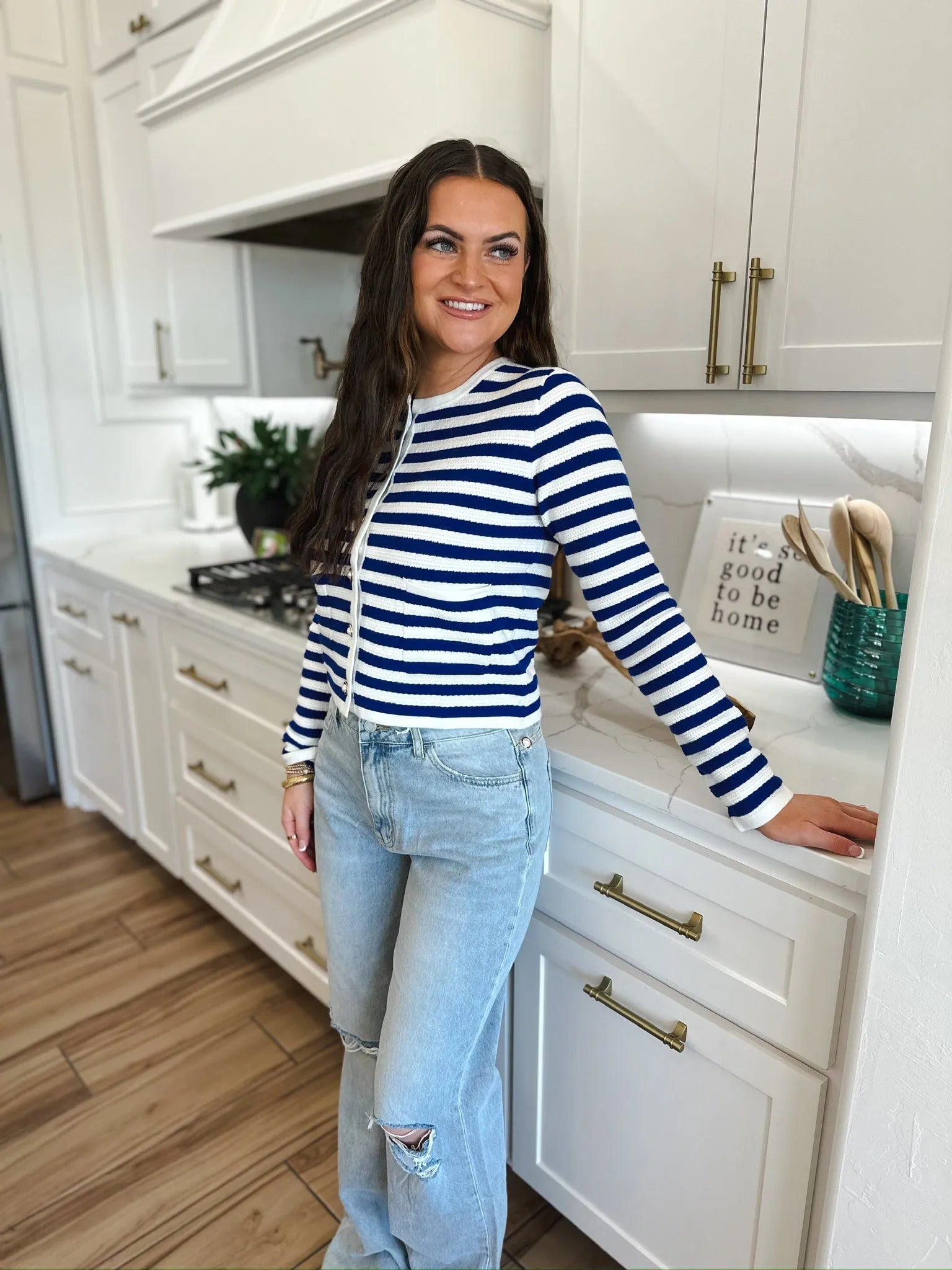 Woman wearing a blue and white striped knit cardigan with pearl buttons and distressed light wash jeans.
