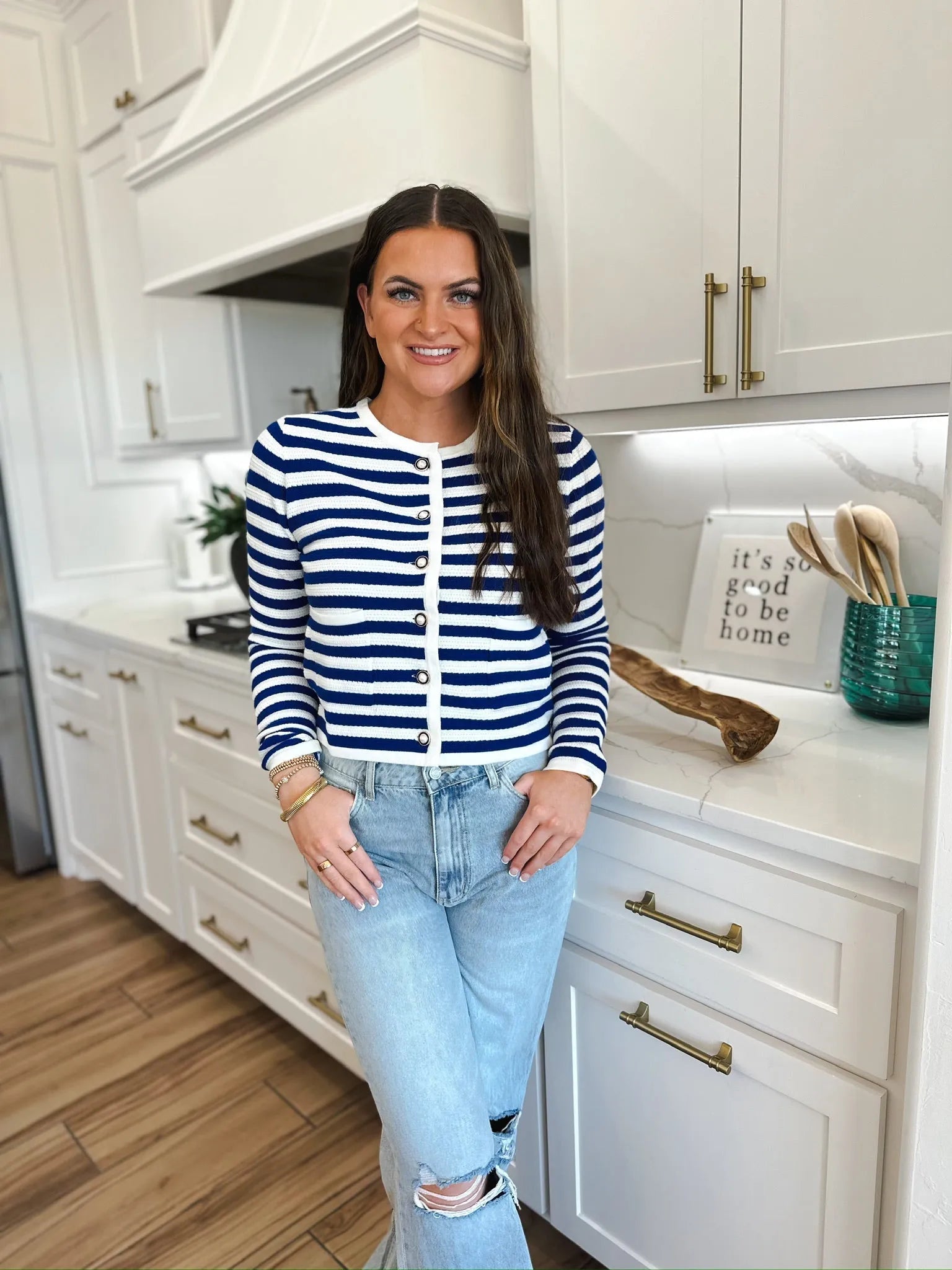 Woman wearing a navy and white striped knit cardigan with pearl buttons and light wash ripped jeans.