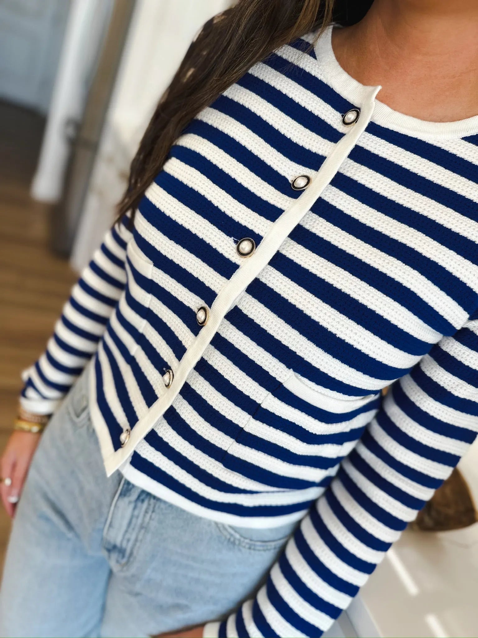 Close-up of a blue and white striped knit cardigan with pearl buttons, featuring a white trim and pocket details.