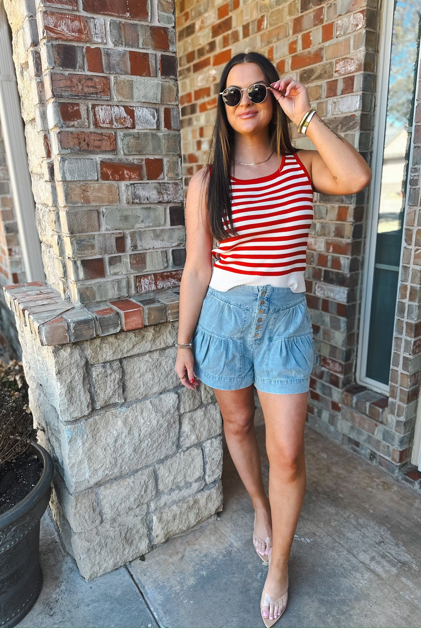 Model wearing mineral washed chambray high waist pleated shorts with button detail and a red and white striped tank top.