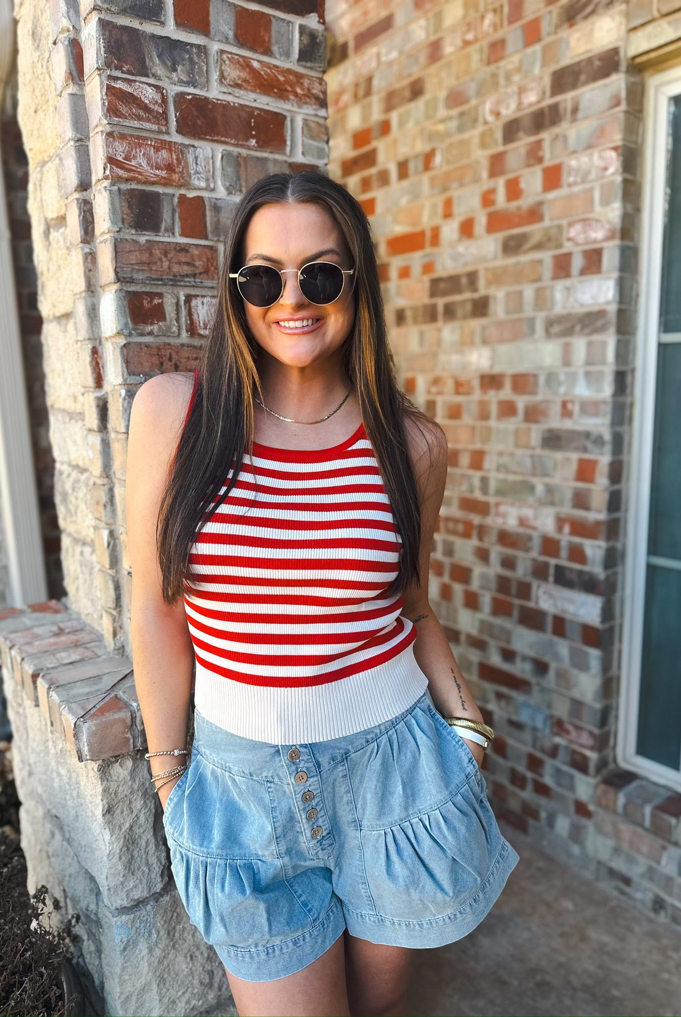 Woman wearing red and white striped tank top and light blue chambray pleated shorts with button front.