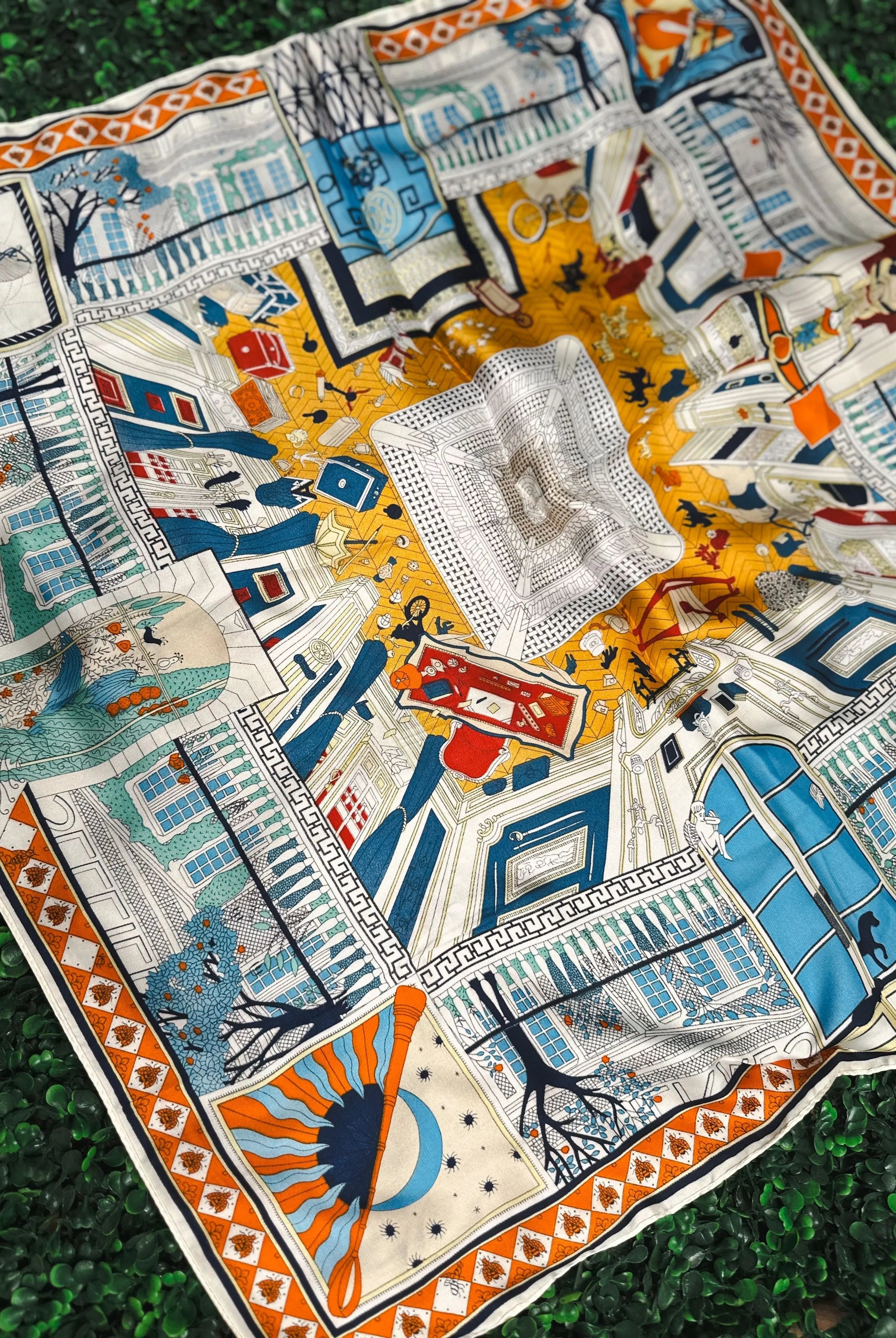 Colorful silk scarf with intricate pattern featuring architectural scenes, trees, sun, moon, and playful figures. Colors